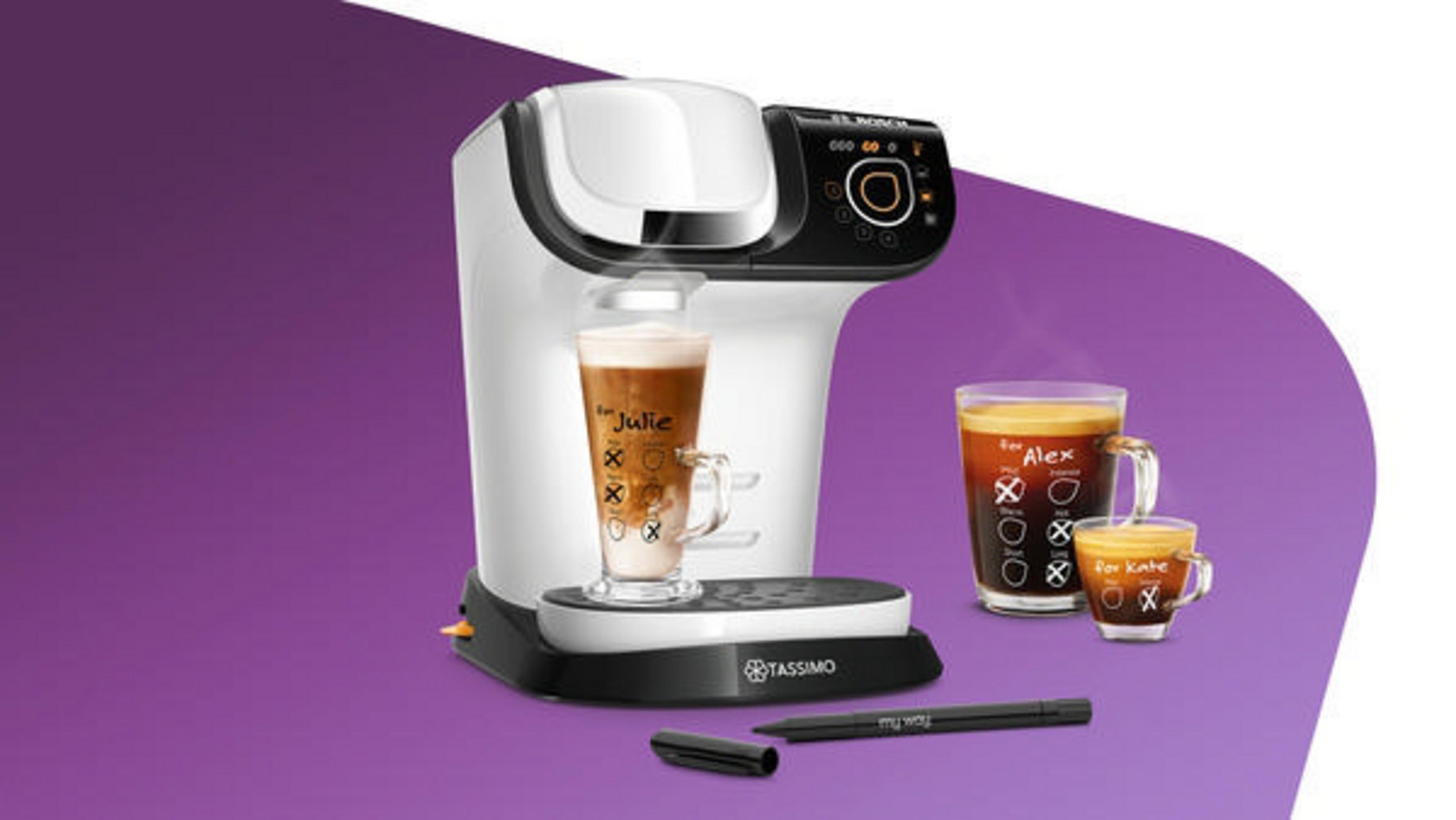 Ekspres do kawy z dwoma filiżankami kawy i długopisem do pisania na filiżankach, na fioletowym tle.