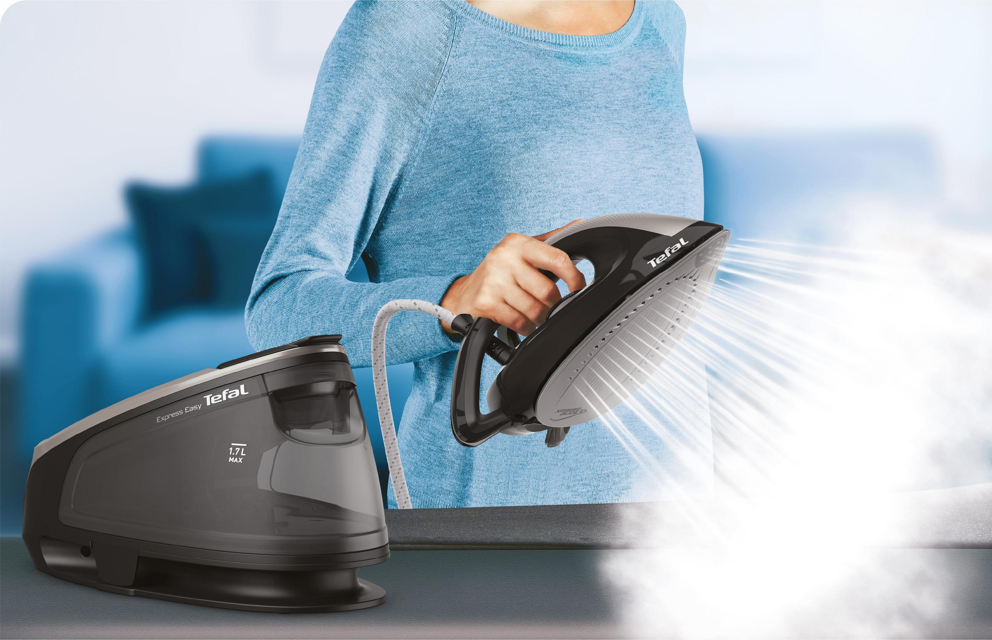 Kobieta prasuje ubrania czarno-szarym żelazkiem, widoczna para.