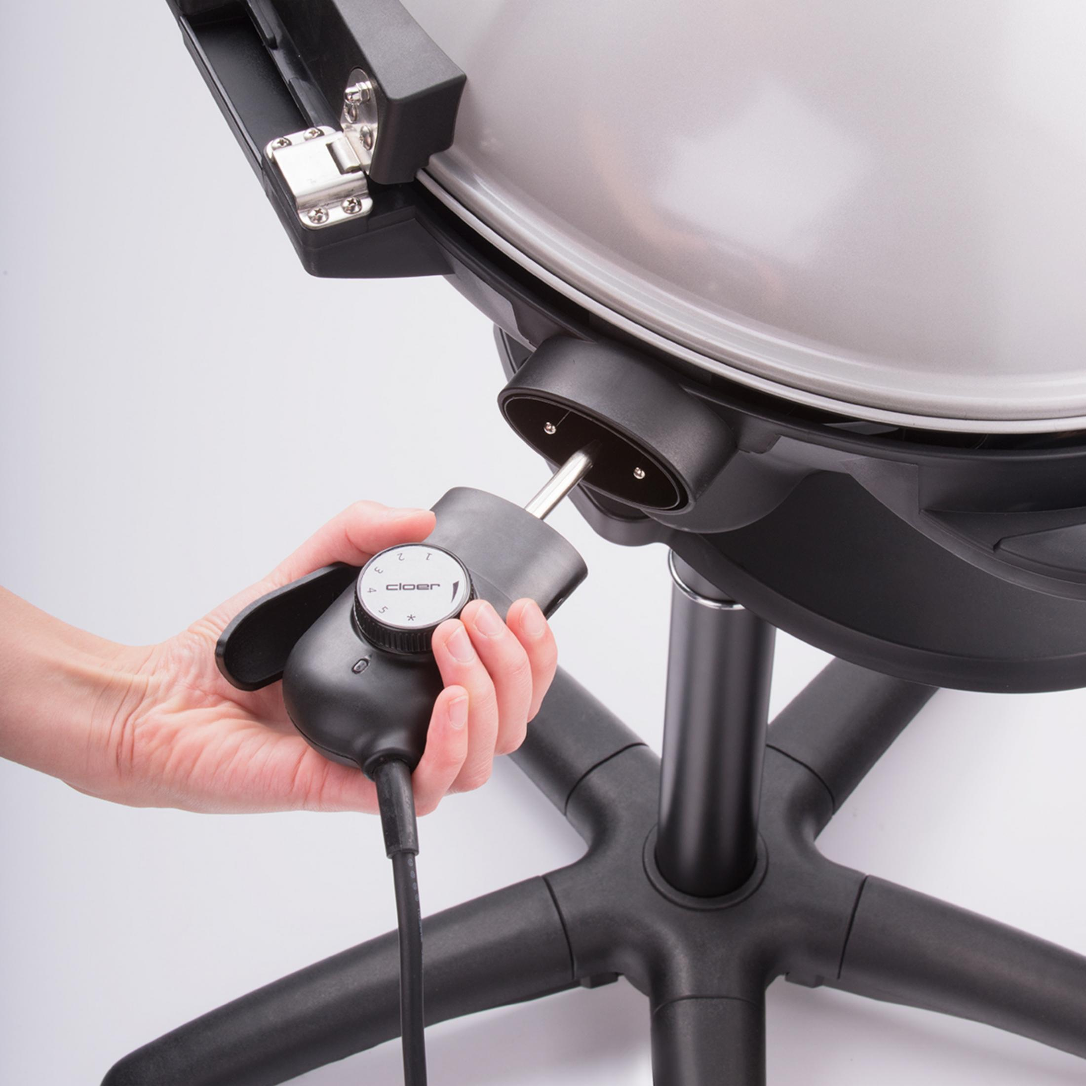 Eine Hand stellt ein schwarzes Bedienfeld an einem silber-schwarzen Grill ein.