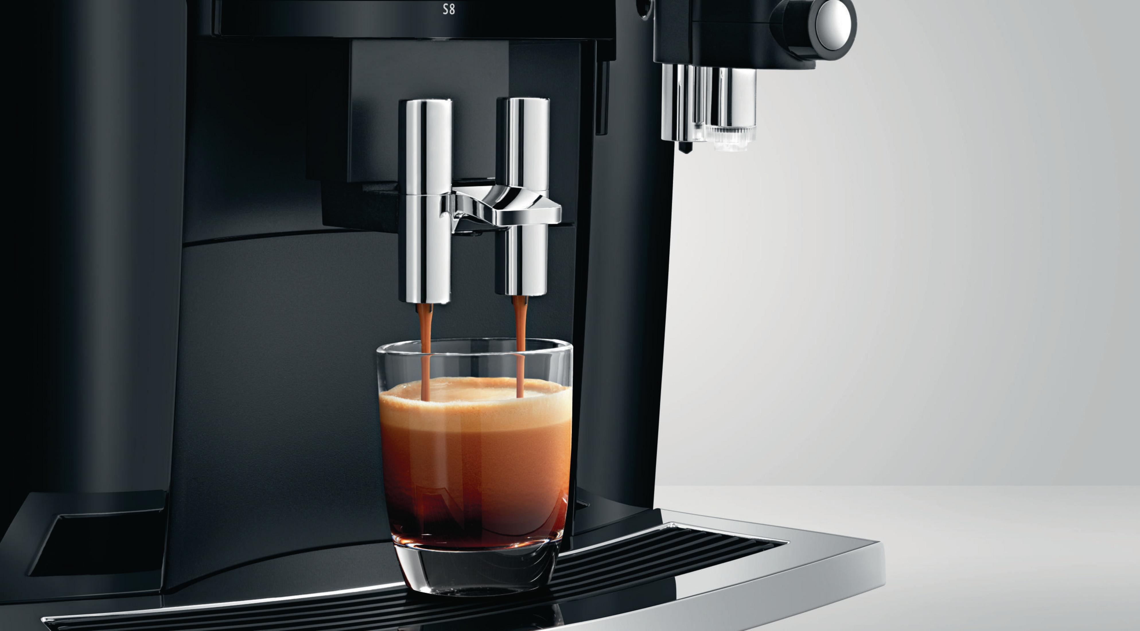 Eine schwarze Espressomaschine, die Kaffee in ein Glas gießt. Der Kaffee ist dunkelbraun mit Schaum.