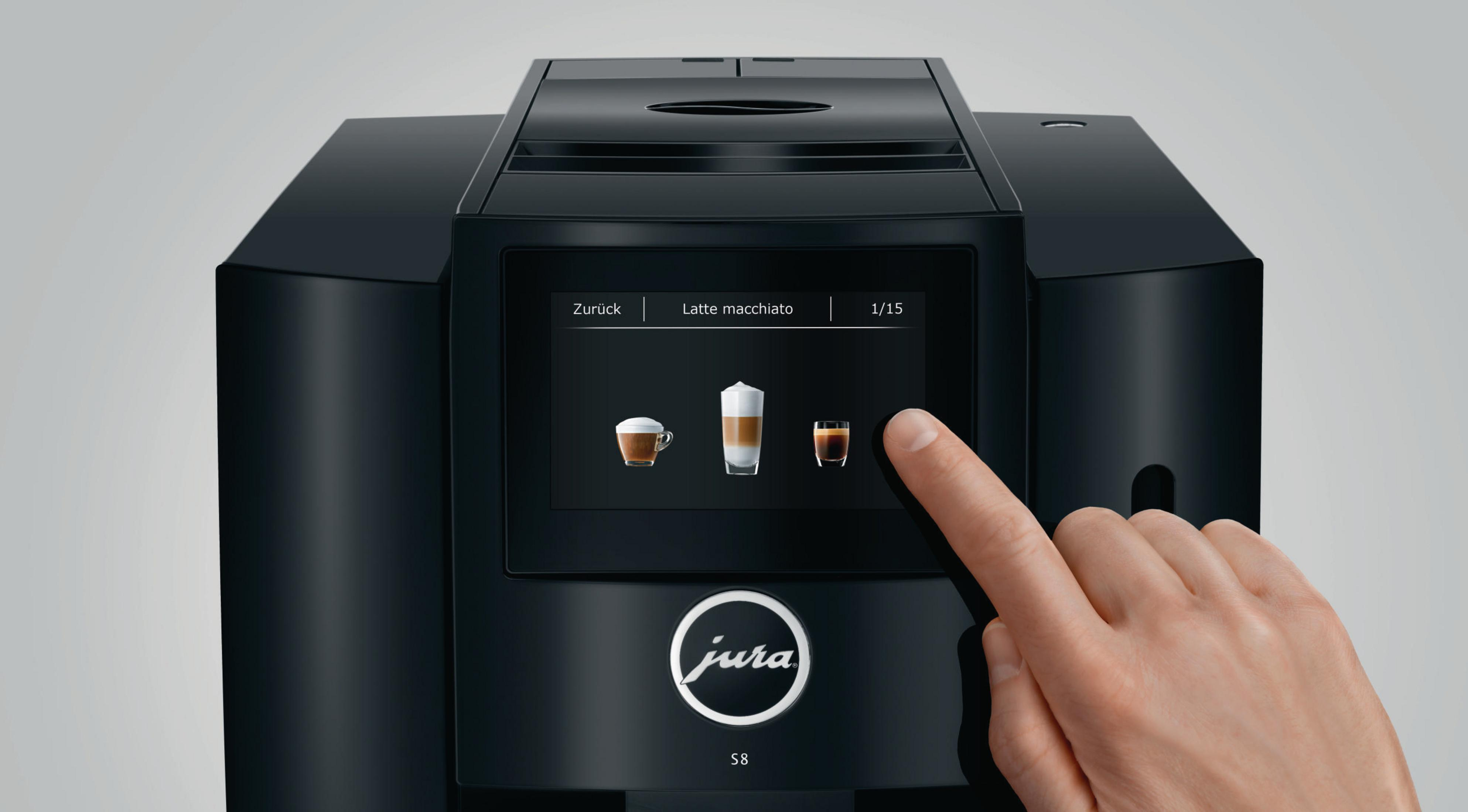 Eine schwarze Kaffeemaschine mit einem Glas Latte Macchiato und einer schwarzen Basis daneben.