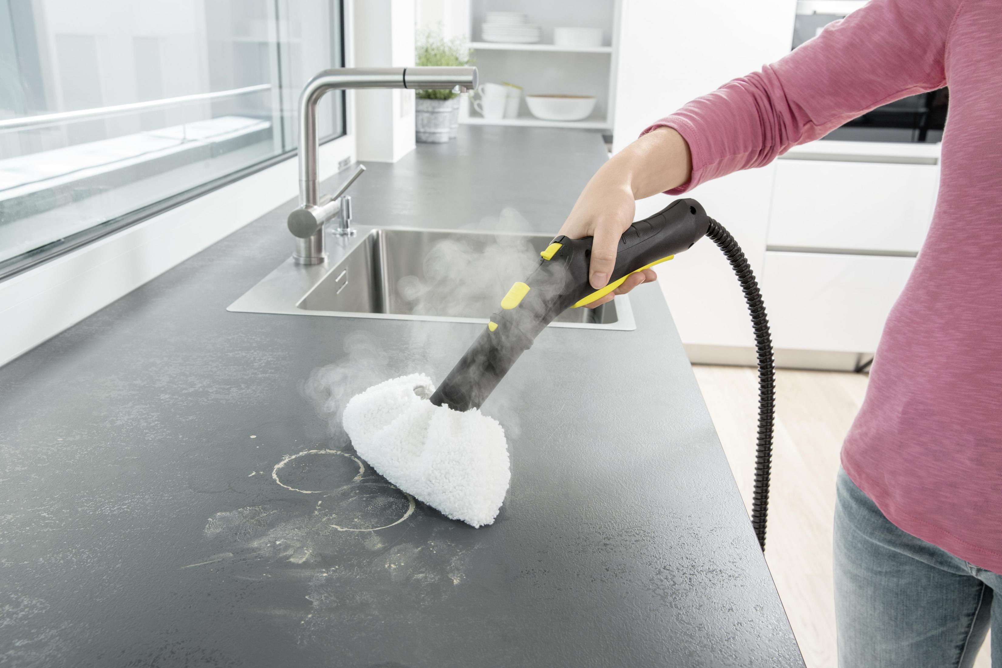 Una persona pulisce un piano di lavoro con un pulitore a vapore, lasciando vapore e segni circolari.