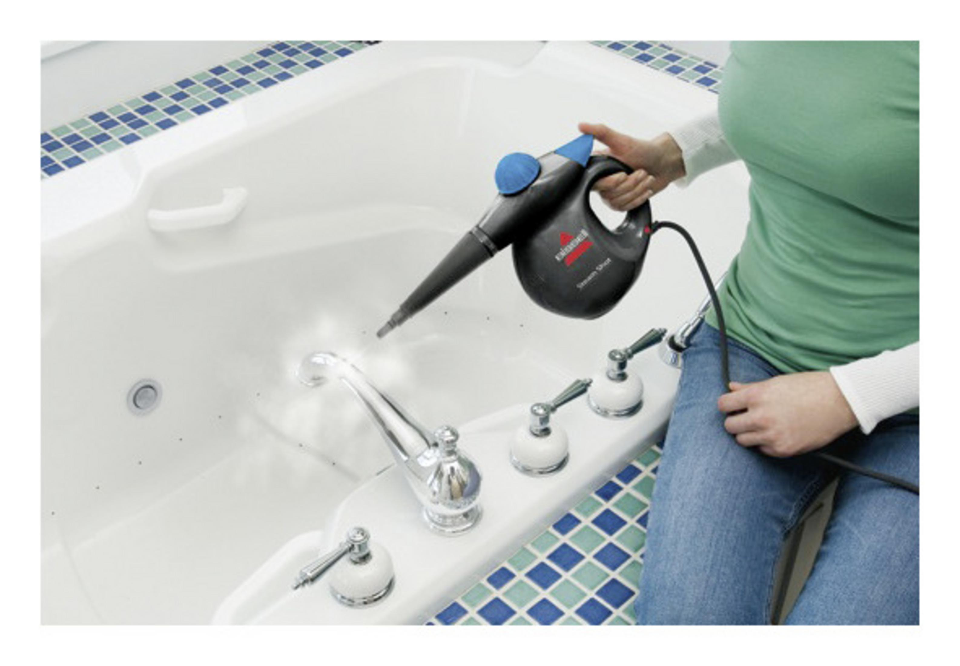 Kobieta czyści białą wannę parownicą. Scena obejmuje krany i niebieskie płytki.