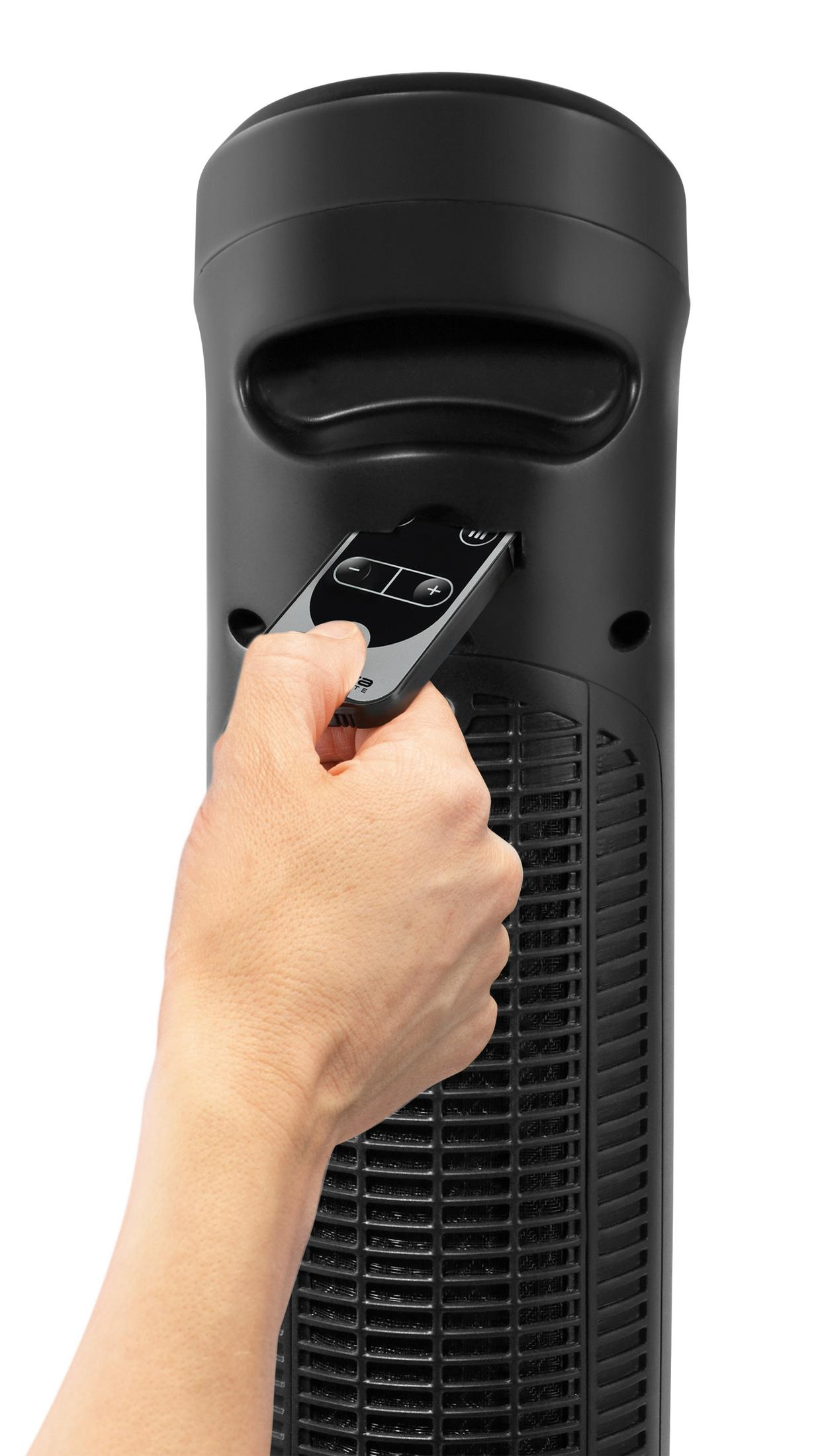 Ręka trzymająca pilota obok czarnego wentylatora wieżowego.