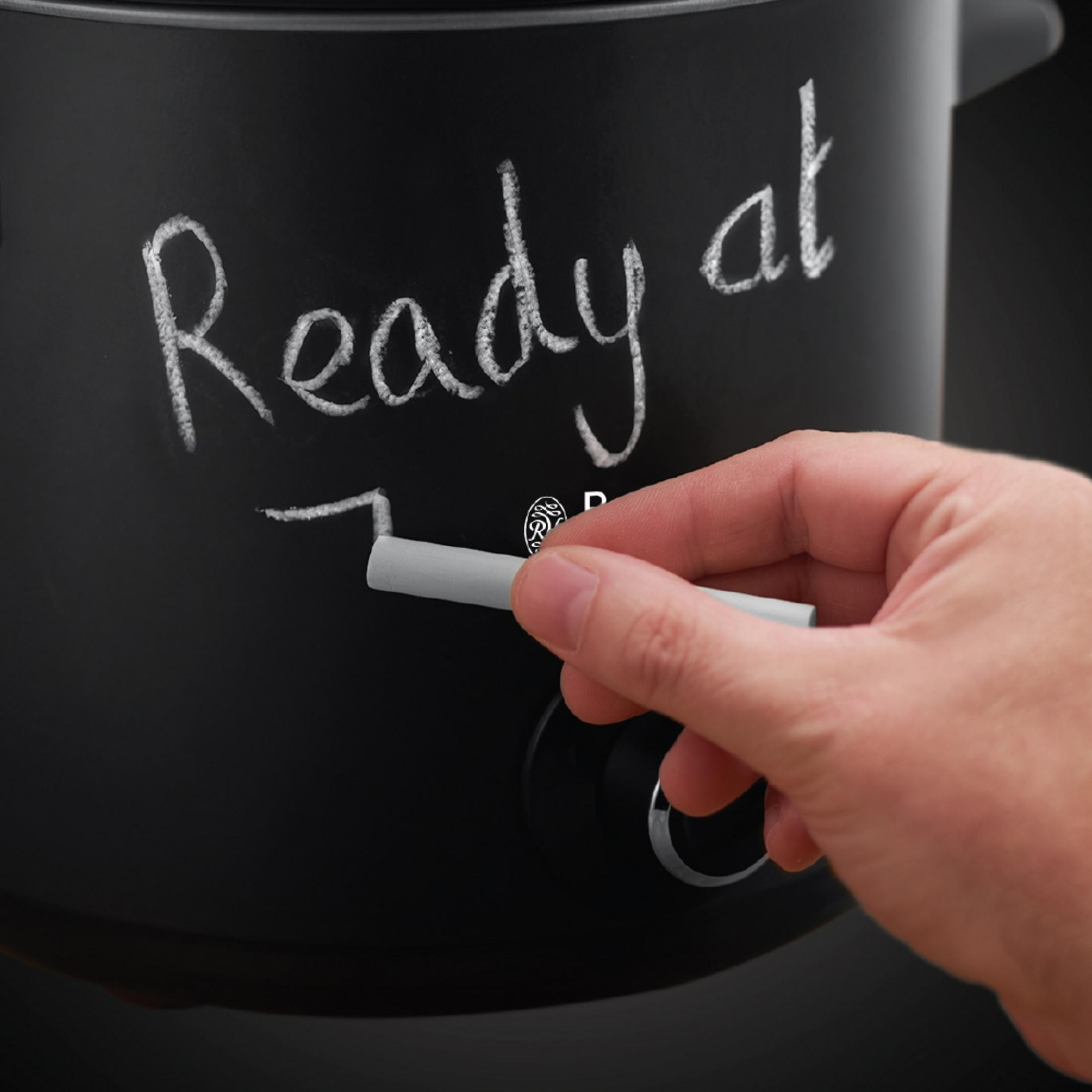 Eine Hand schreibt mit Kreide 'Ready at 7' auf einen schwarzen Slow Cooker.