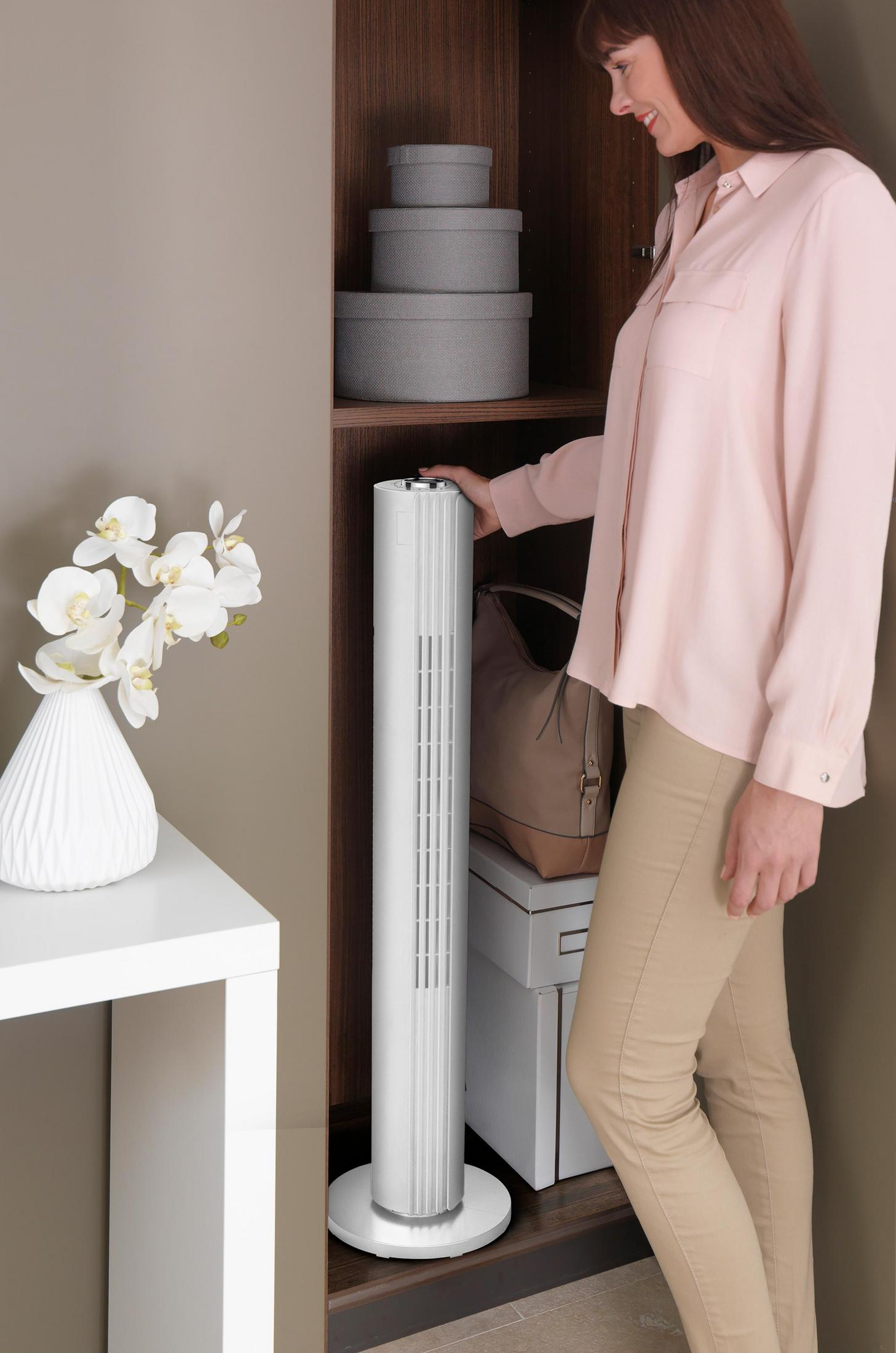 Mujer abriendo armario con ventilador blanco, flores y cajas dentro.
