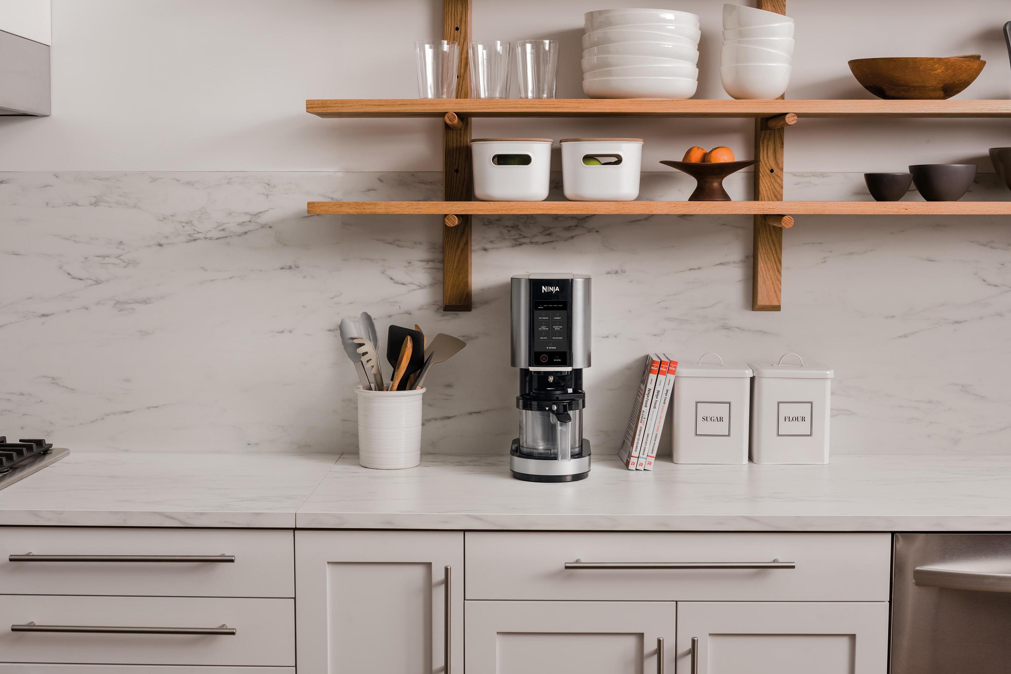 Scena kuchenna z ekspresem do kawy Ninja na blacie, różne naczynia na półkach i blacie.
