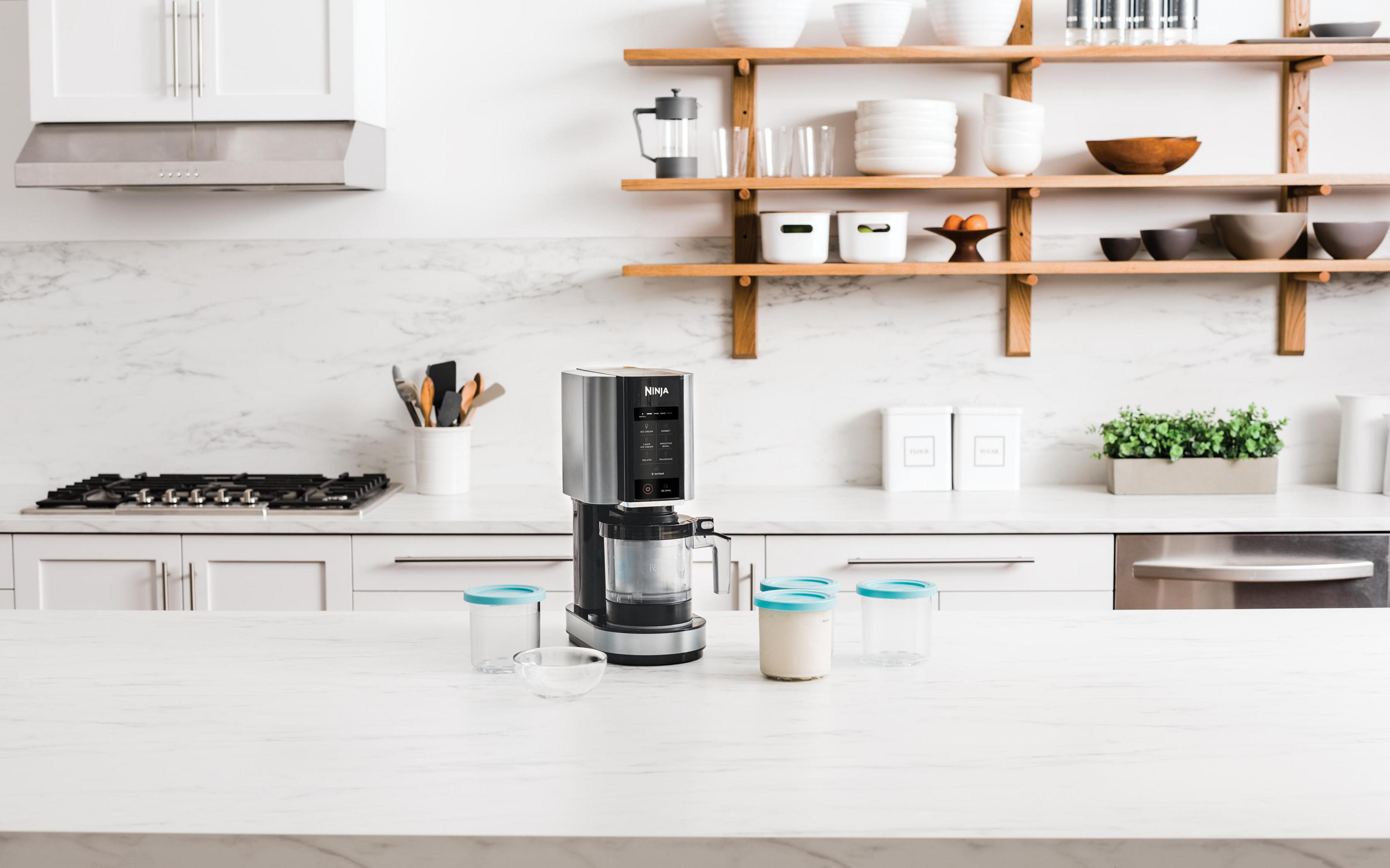 Blat kuchenny z maszyną do lodów Ninja i akcesoriami. Białe tło.