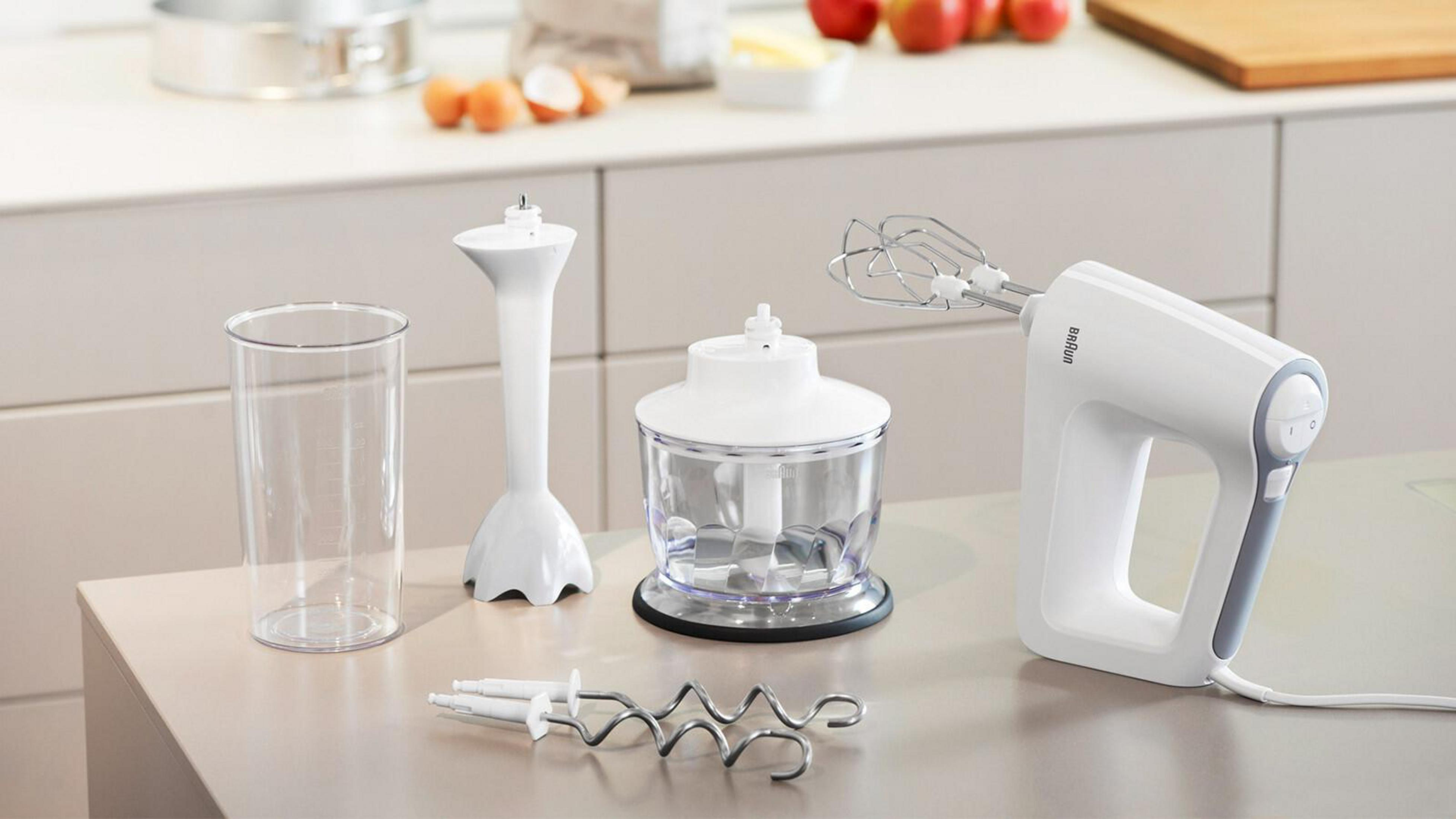 Een set keukengereedschap, waaronder een blender, een handmixer en opzetstukken, op een aanrecht.