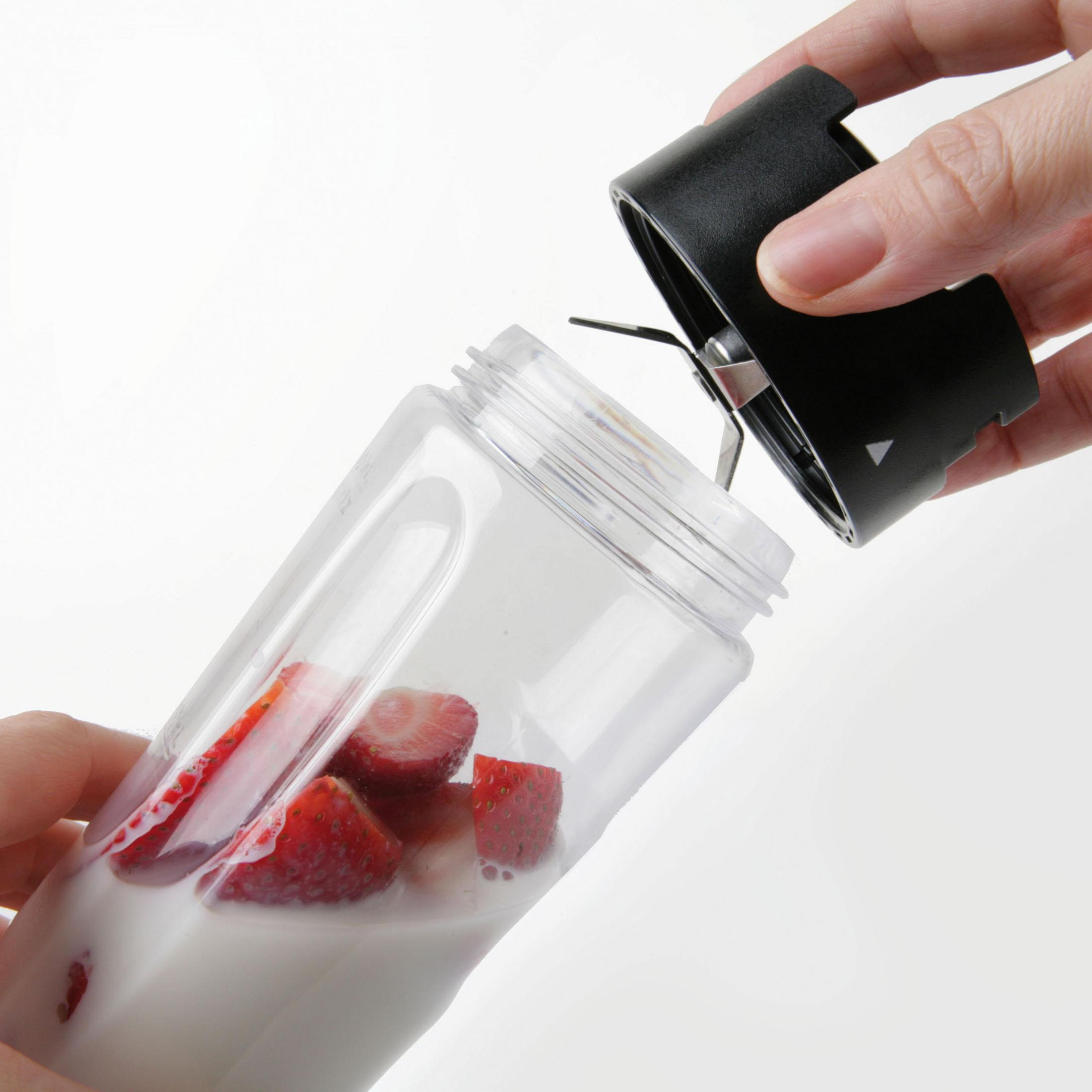 Eine Hand, die einen Mixer mit Erdbeeren und Milch zusammensetzt.