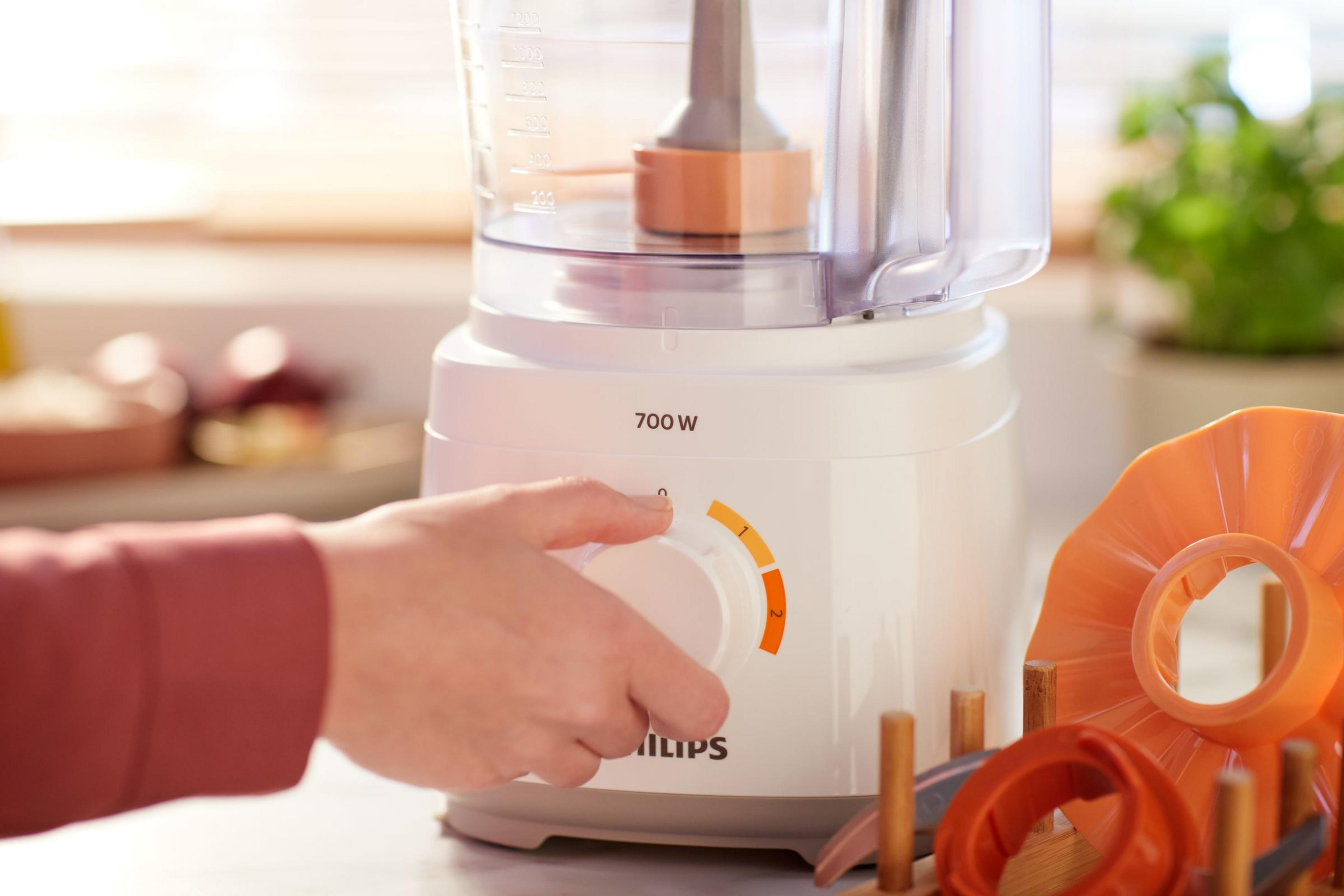 Hand adjusting food processor dial. White appliance with orange elements.