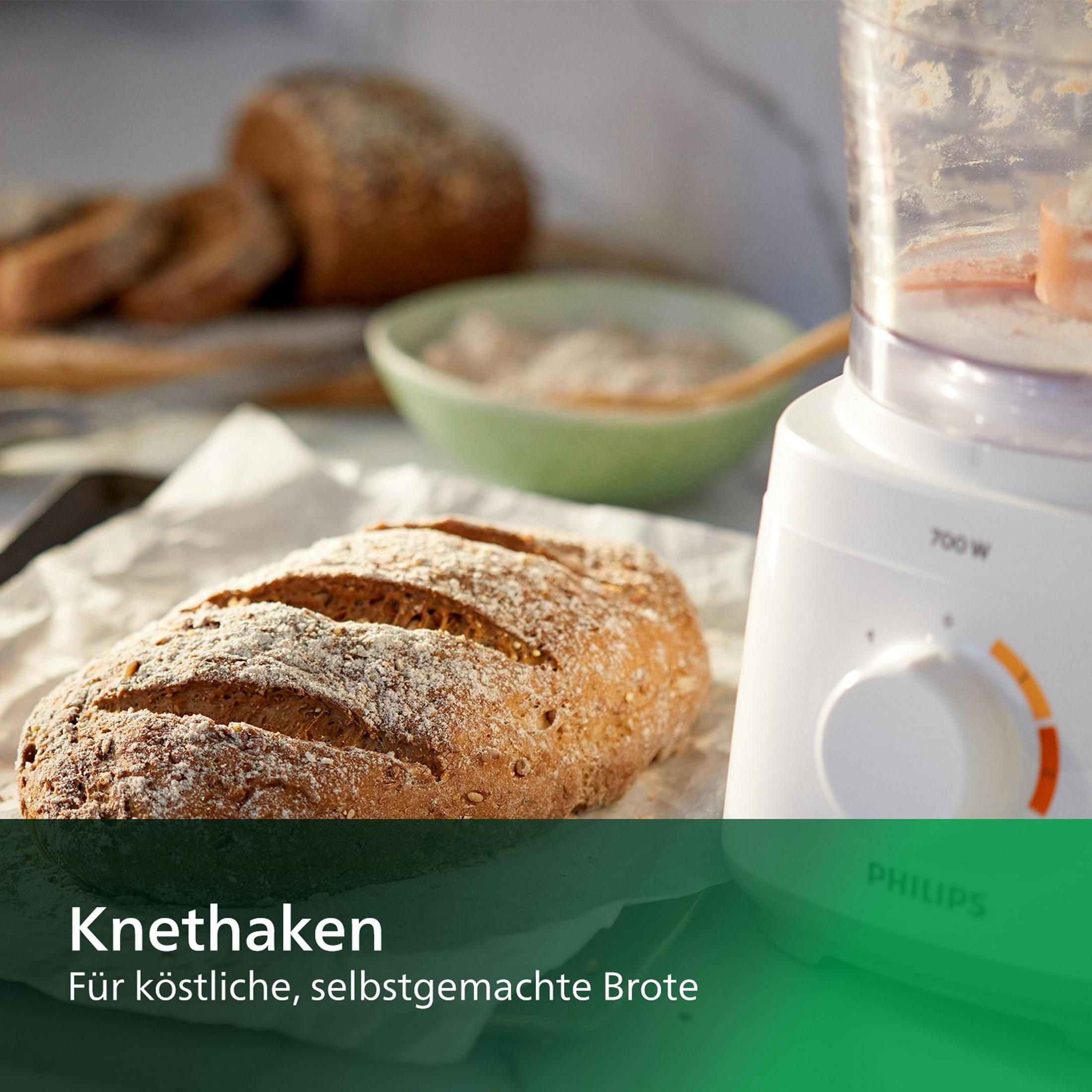 A loaf of bread and a food processor. The bread is on white paper, scattered with flour.