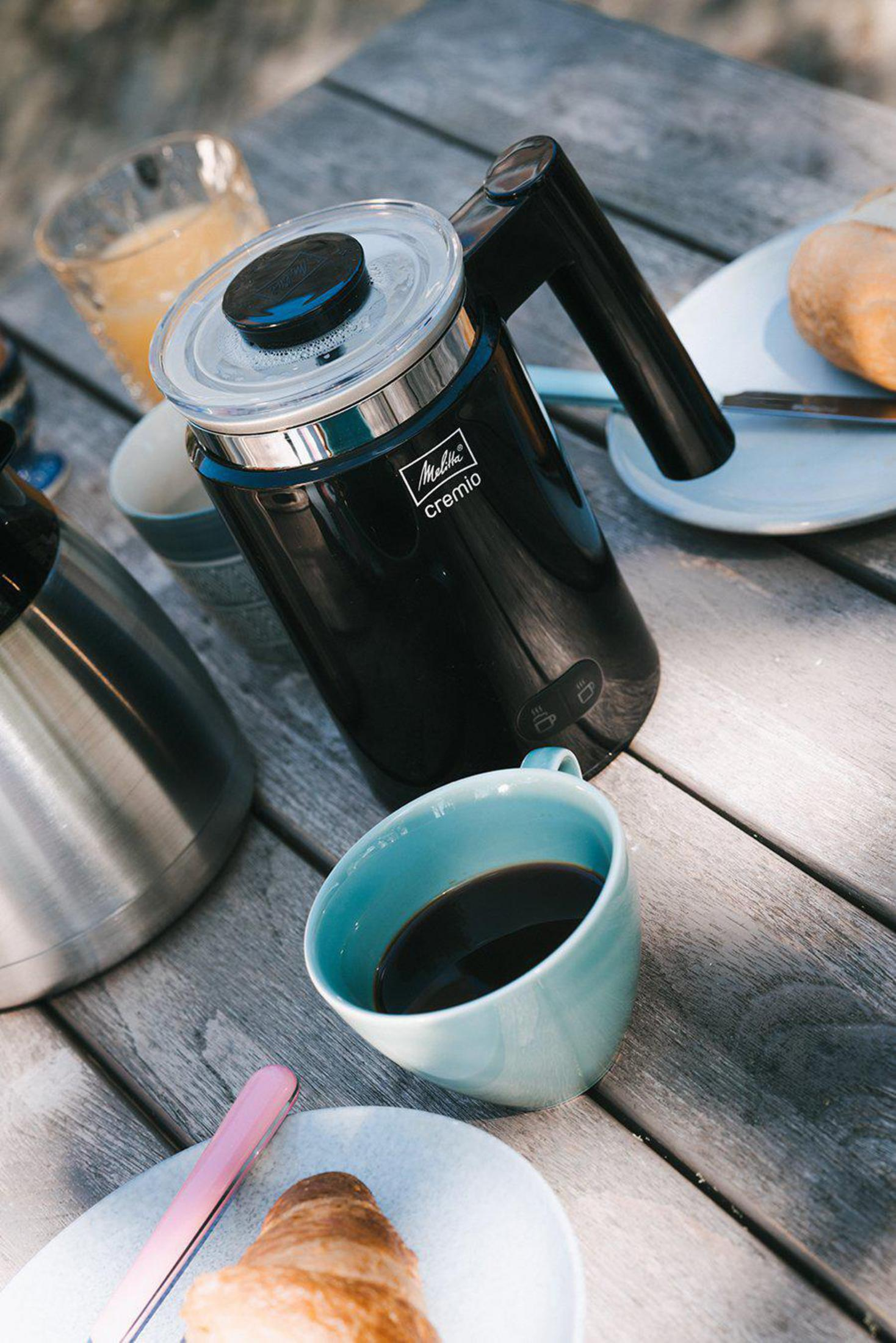 Ekspres do kawy i filiżanka kawy na drewnianym stole z jedzeniem.