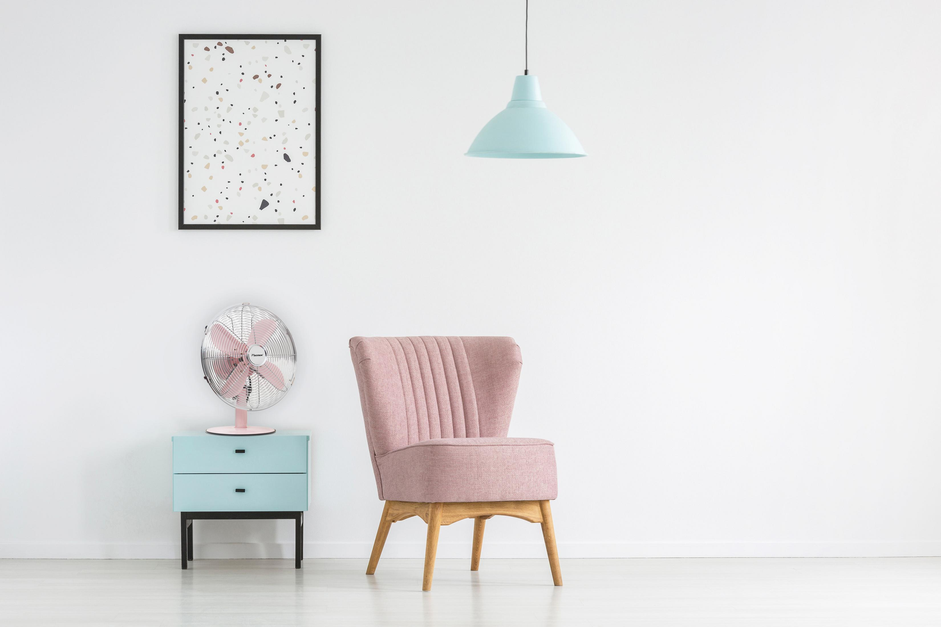 Stanza con sedia rosa, ventilatore, armadietto, quadro e lampada blu.