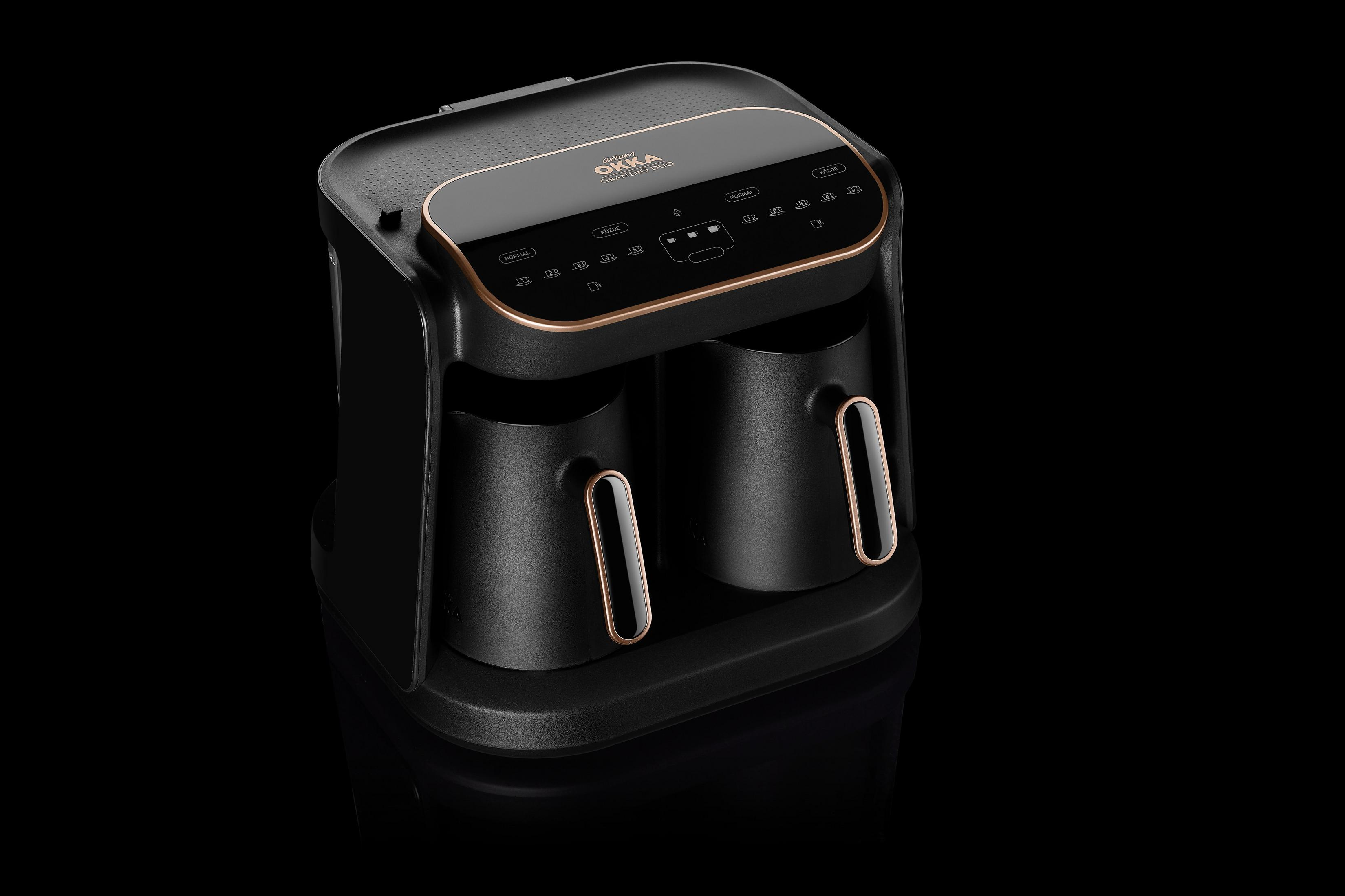 Czarny ekspres do kawy ze złotymi akcentami, oznaczony 'OKKA'. Maszyna stoi na czarnej, odblaskowej powierzchni.