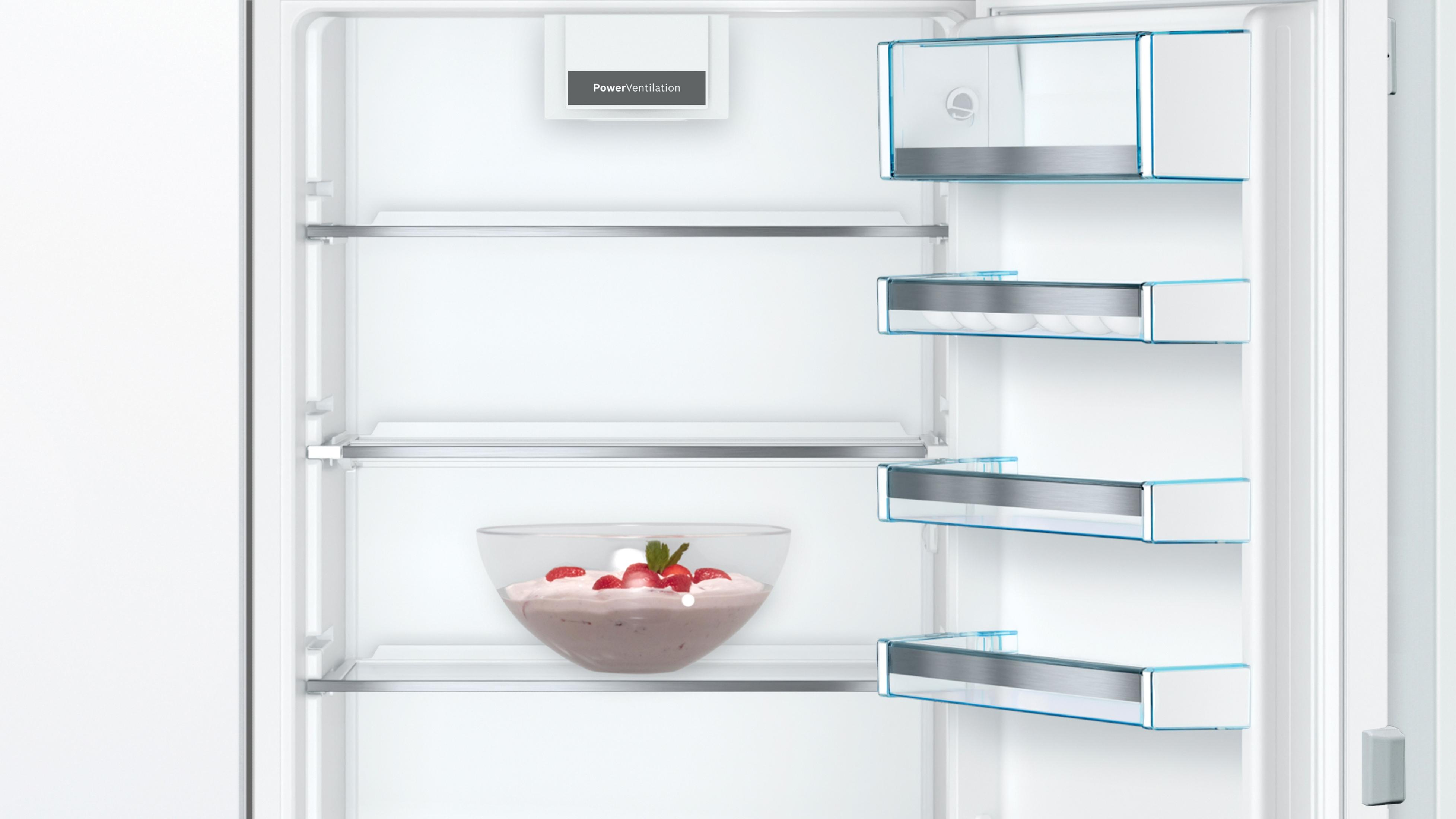 Interior de refrigerador con estantes. Un cuenco de postre rosa con fresas está en un estante.