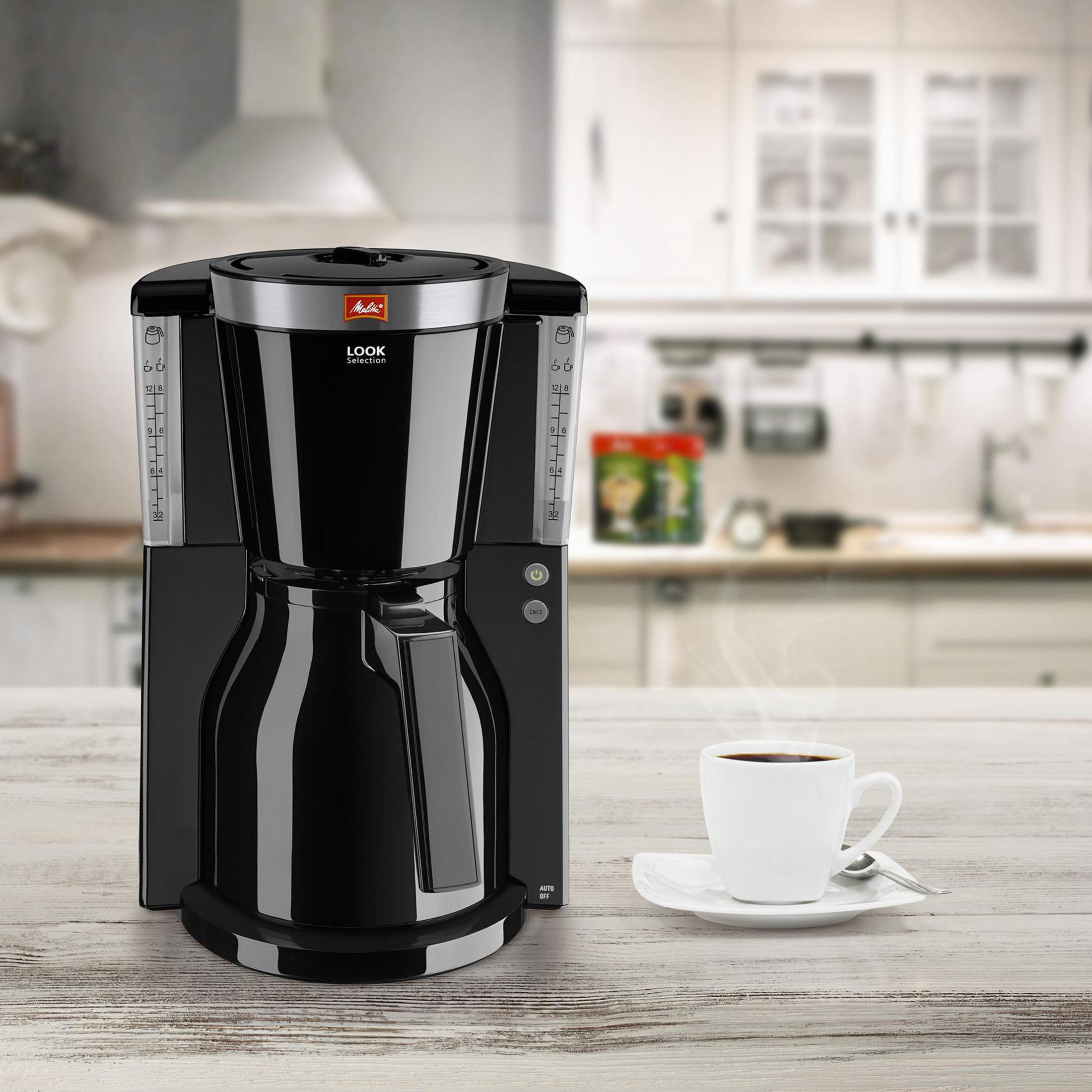 Una cafetera negra con una taza de café blanca sobre una superficie de madera.