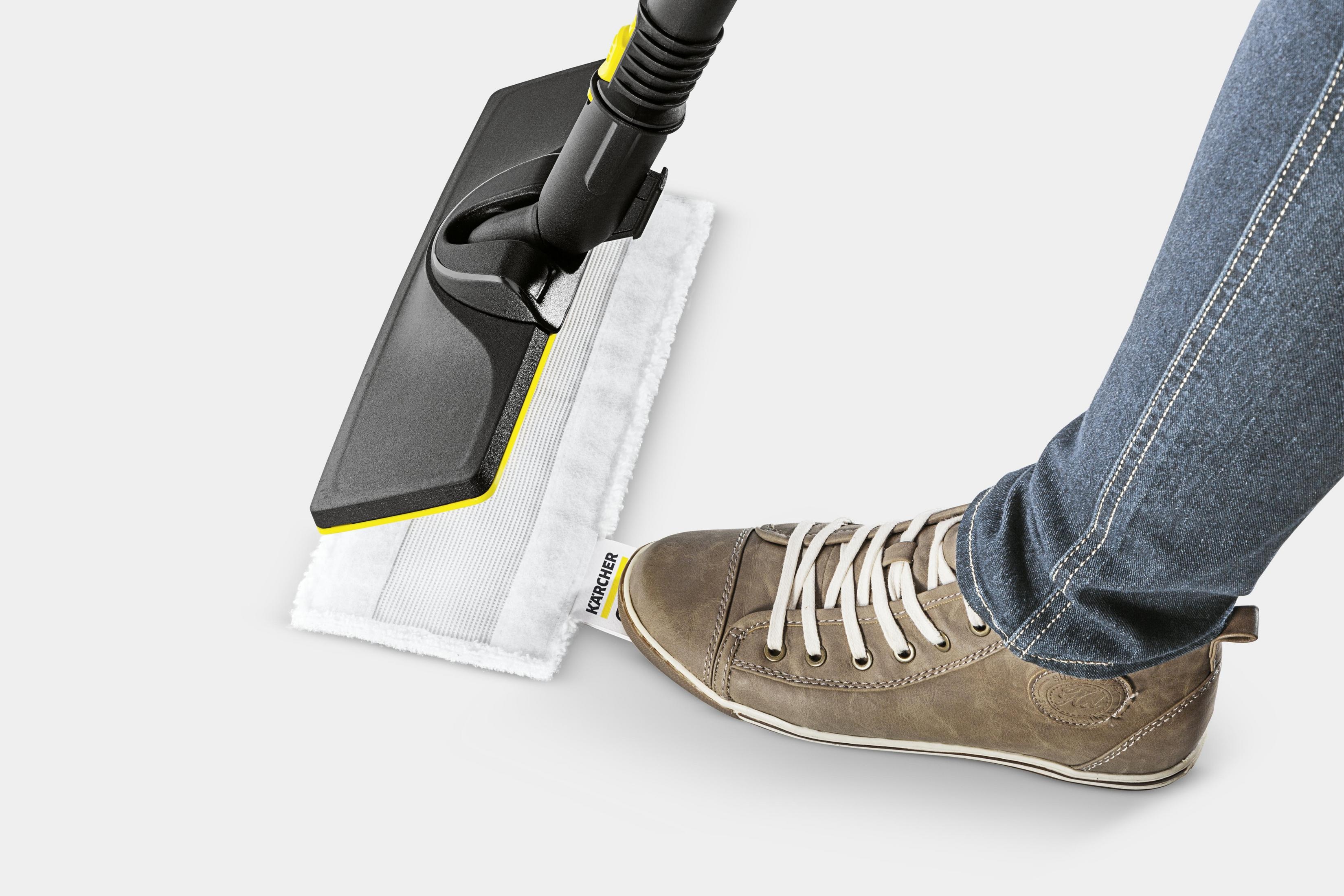 Piede di persona vicino a un pulitore a vapore. Jeans e scarpa casual. Sfondo bianco.