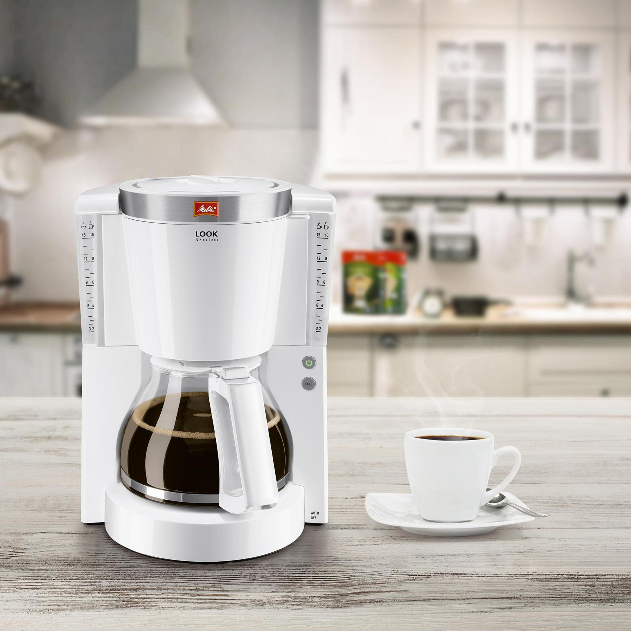 Una macchina per il caffè bianca con una caraffa di vetro piena e una tazza di caffè accanto.