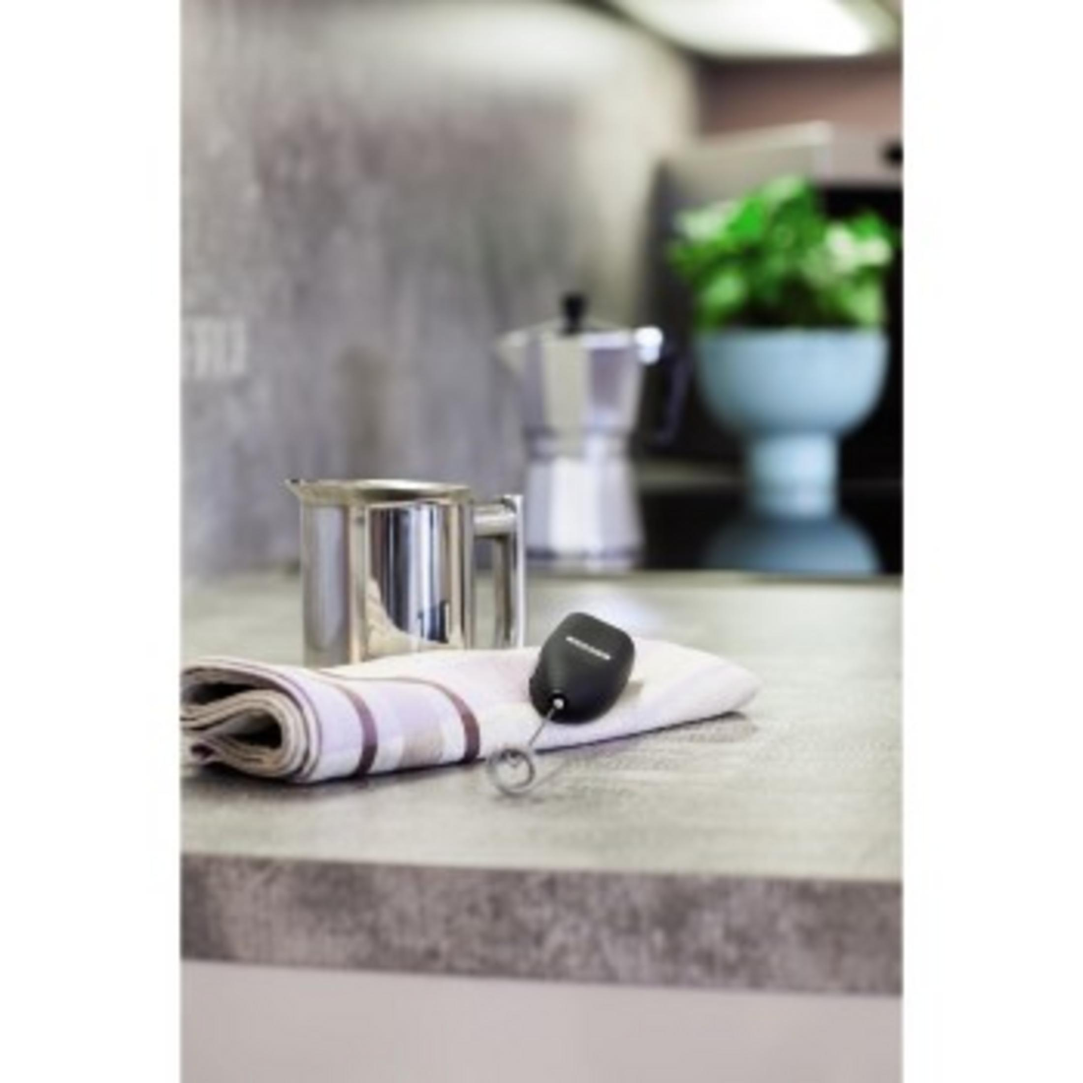 Scena na blacie kuchennym. Kubek ze stali nierdzewnej, kawiarka, spieniacz i ręcznik. Zielona roślina w tle.