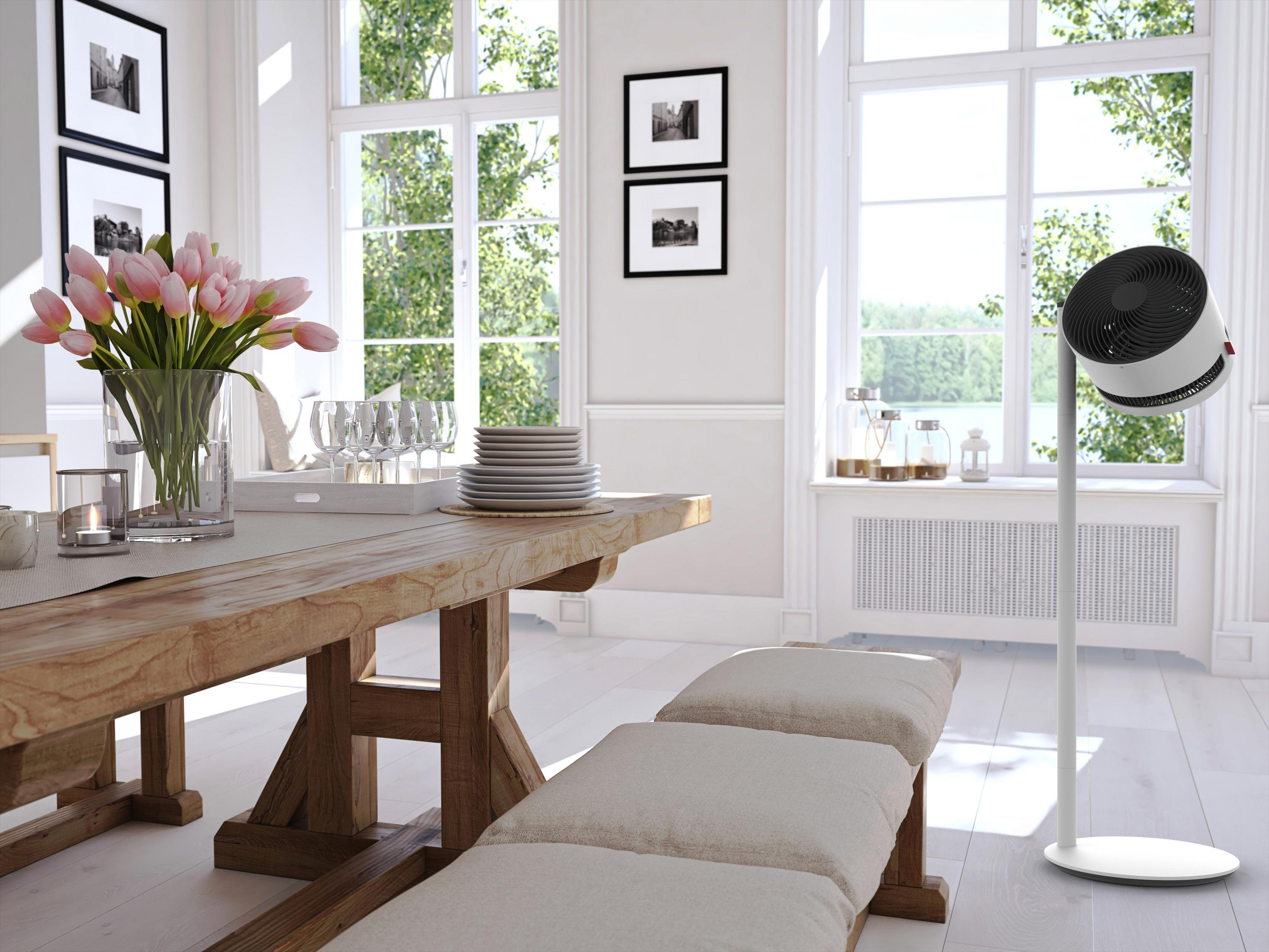 Chauffage soufflant blanc et moderne sur pied dans une pièce ensoleillée avec une table à manger et un banc.
