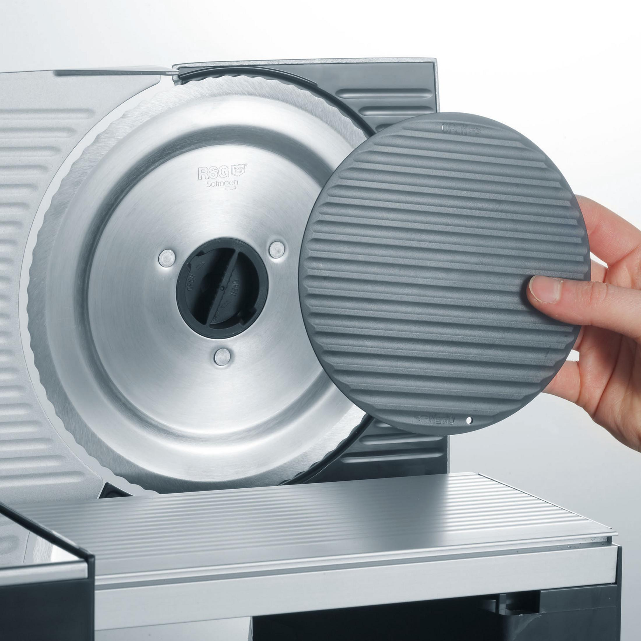 Ręka trzymająca szarą, żebrowaną tarczę obok srebrnej krajalnicy do żywności.