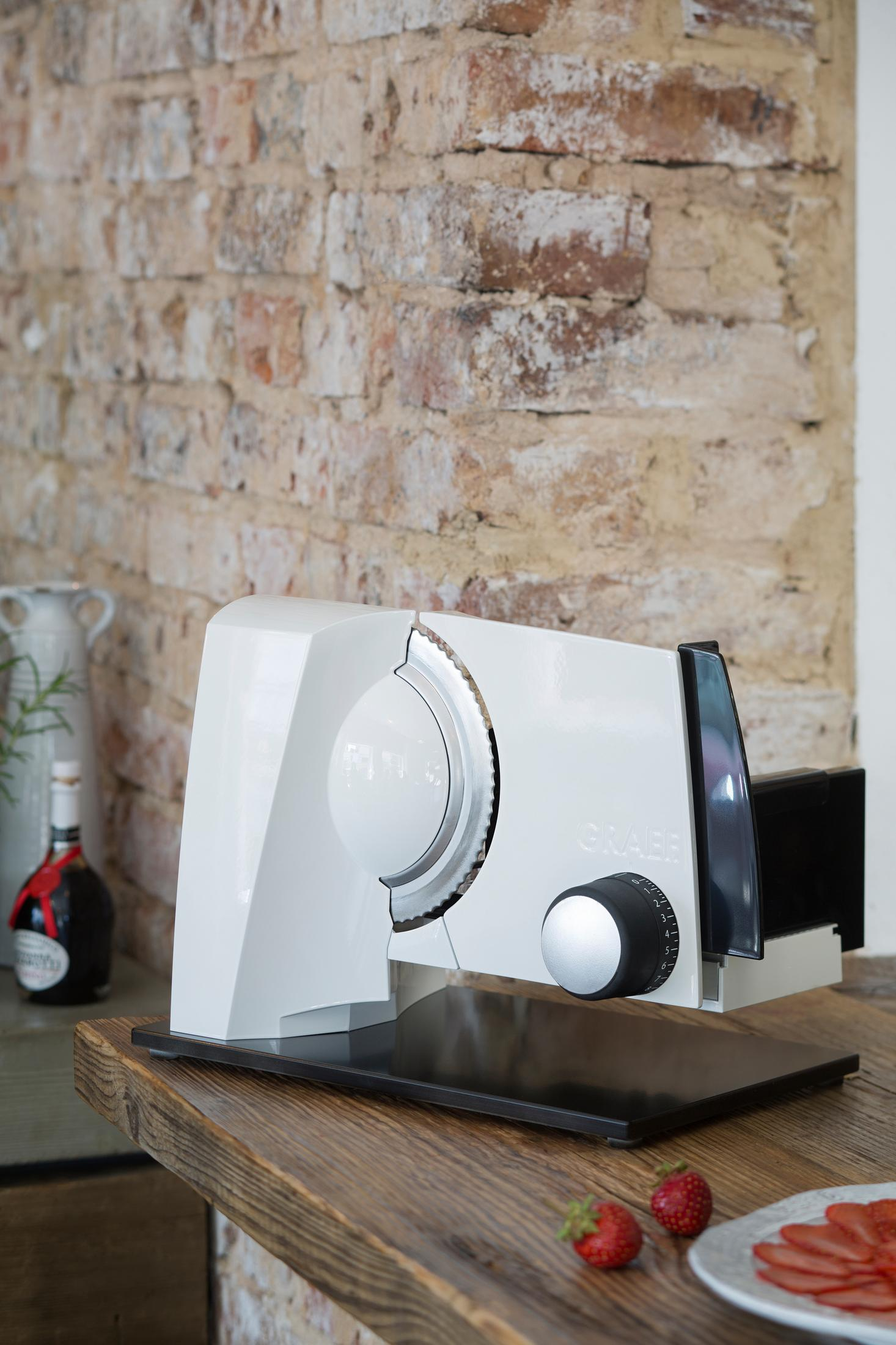 Biała krajalnica do żywności na drewnianej powierzchni, z tłem z czerwonej ceglanej ściany.