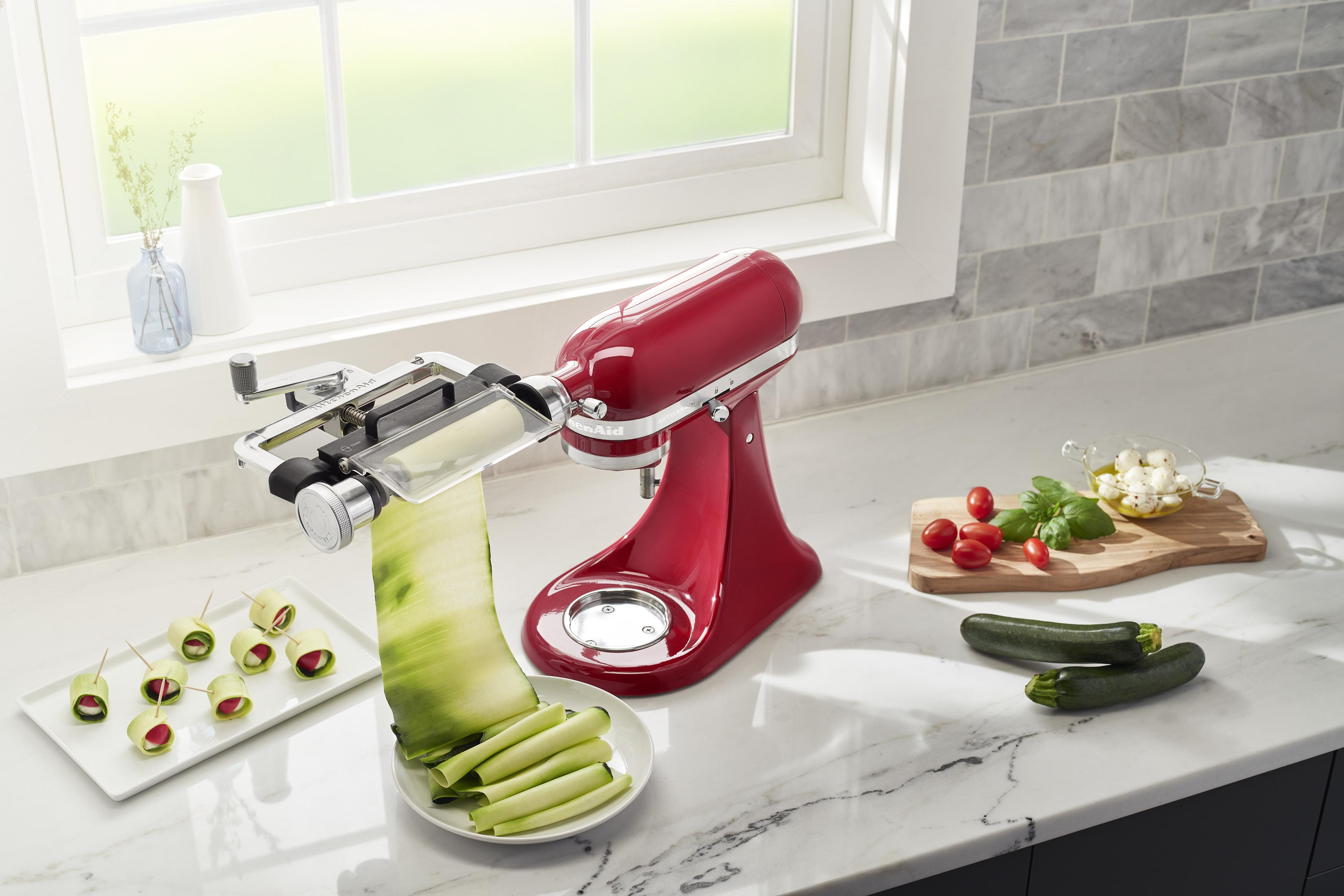 Roter KitchenAid-Mixer mit Gemüsespiralschneider, Zucchini und Tomaten auf der Theke.