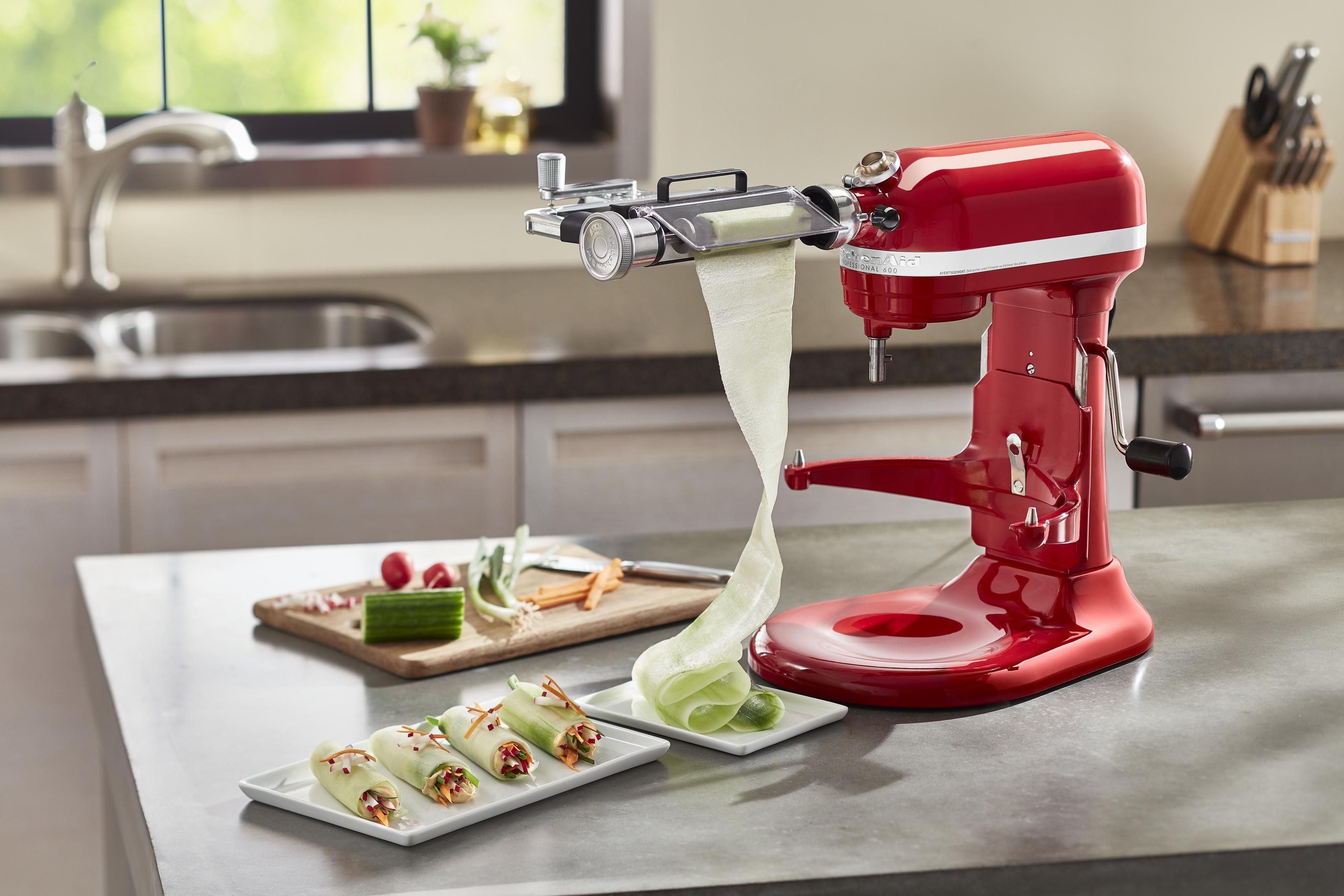 Roter Küchenmixer mit Gemüse-Spiralschneider-Aufsatz, der Zucchin Nudeln herstellt. Rollen im Vordergrund.