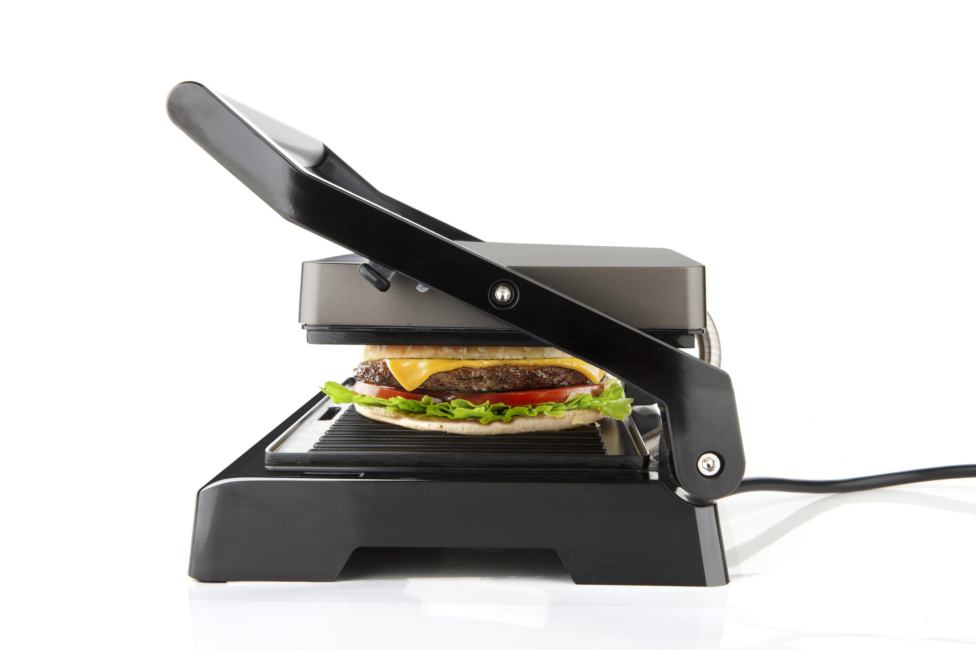 Ein geschlossener Grill mit einem Hamburger darin, auf einer weißen Oberfläche.