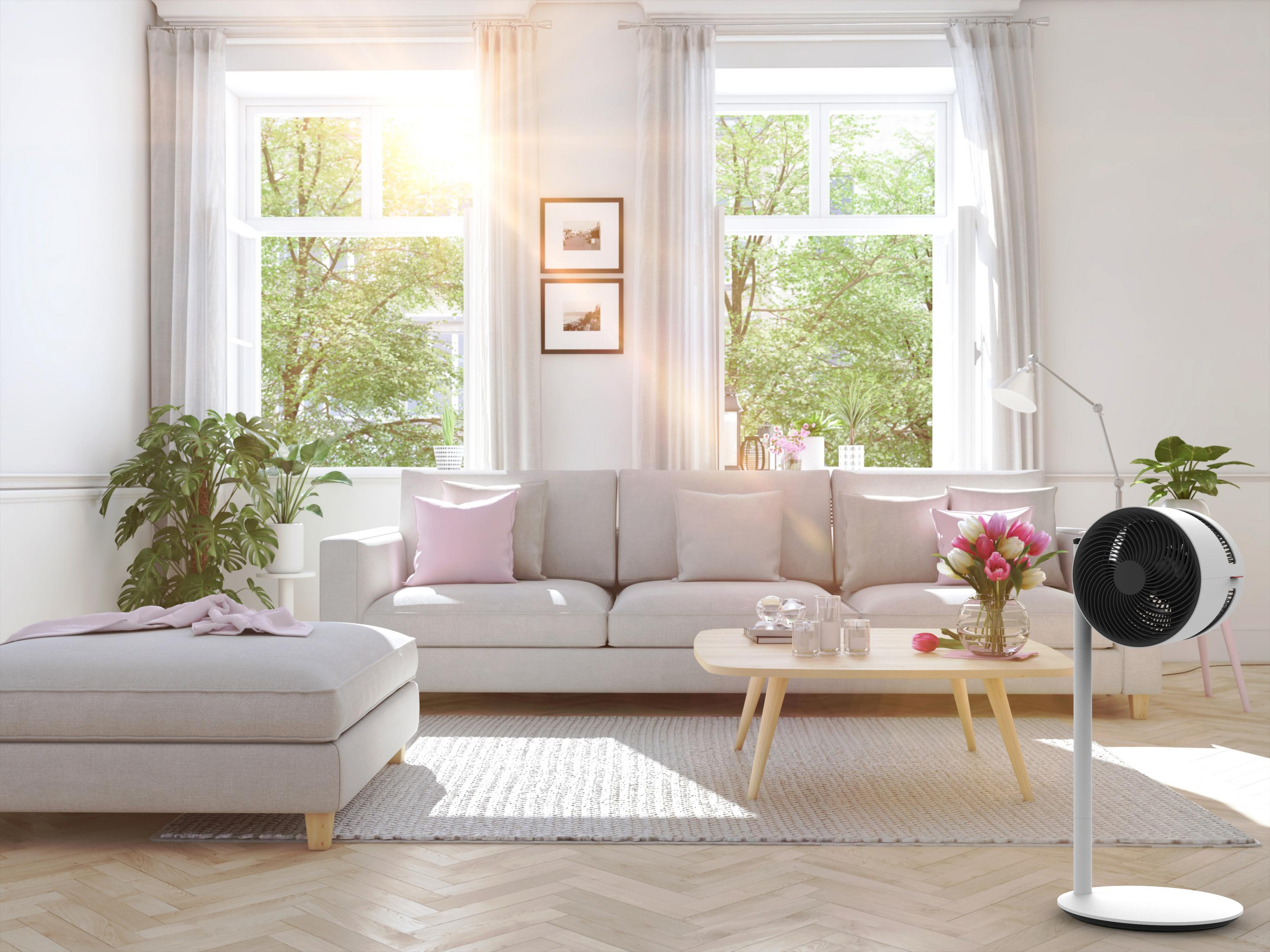 Une scène de salon avec un canapé, une table basse, un ventilateur et de grandes fenêtres.