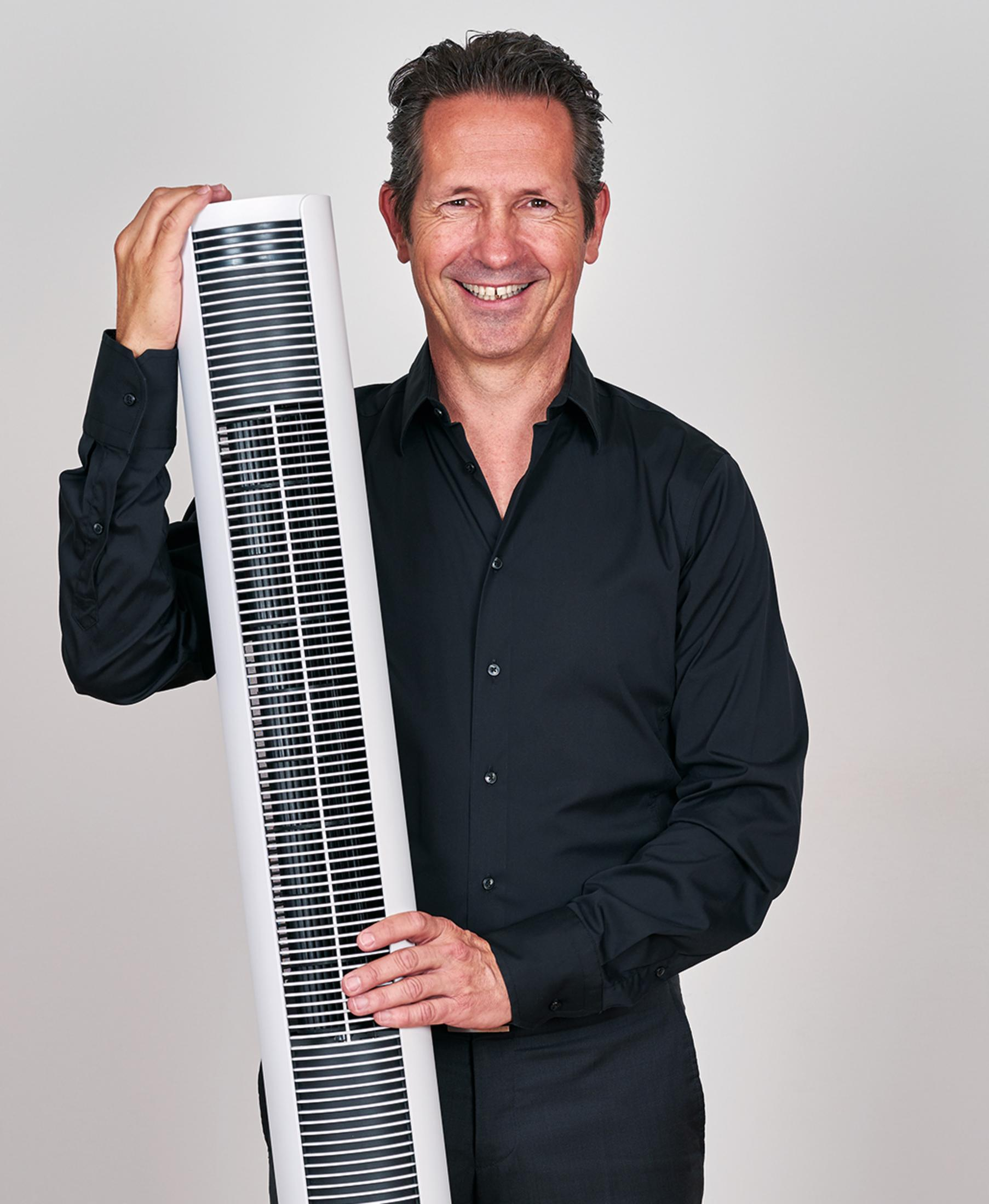 Un homme en chemise noire tient un grand purificateur d'air blanc.