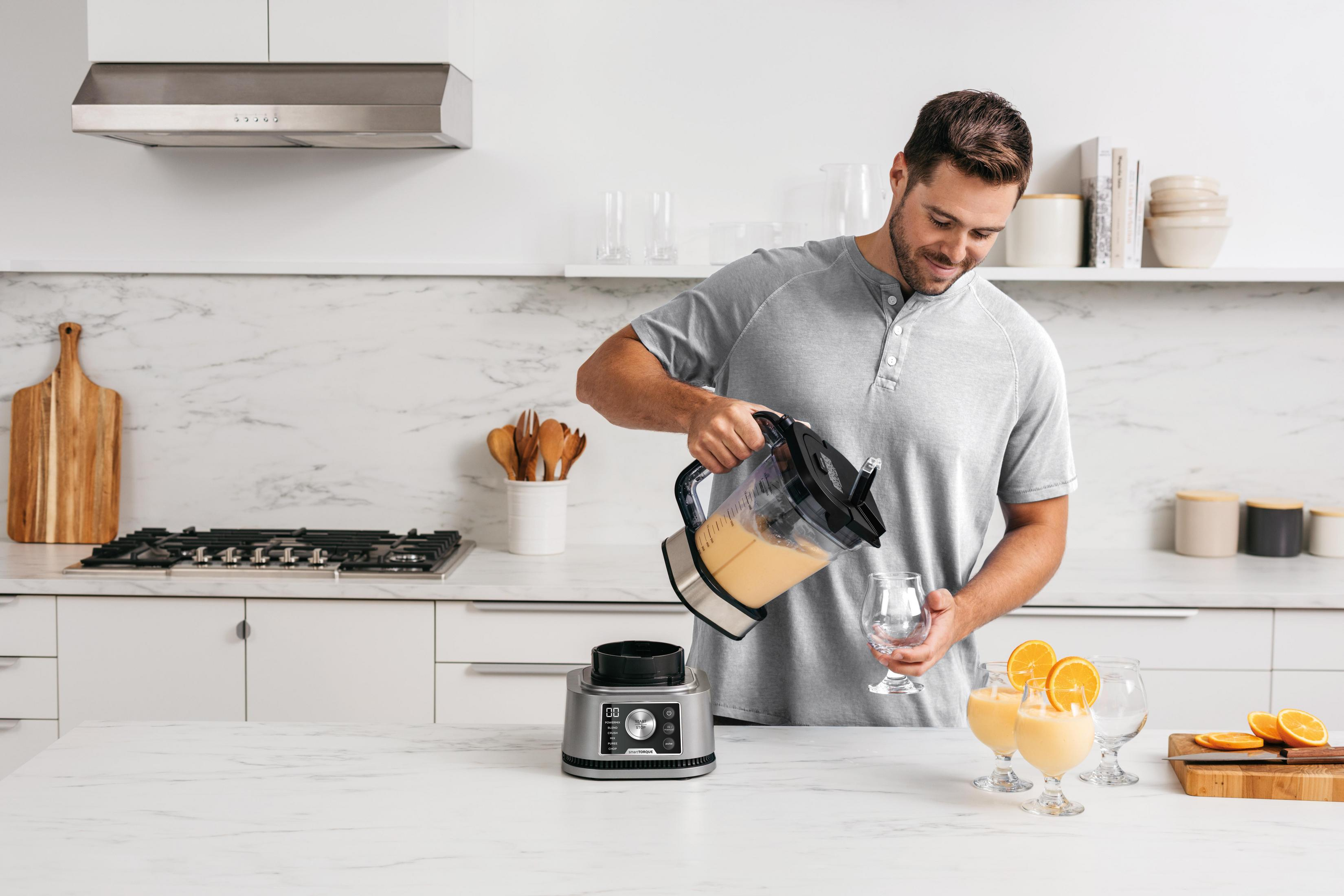 Man pouring a smoothie into glasses next to a blender with cut oranges.