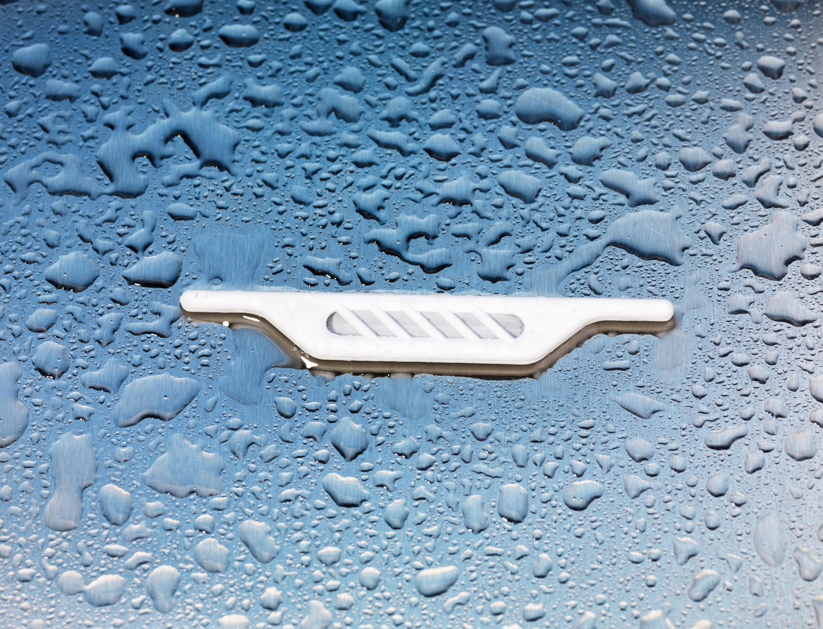 Pièce en plastique blanc avec rainures sur surface bleue et mouillée. Gouttes d'eau visibles.