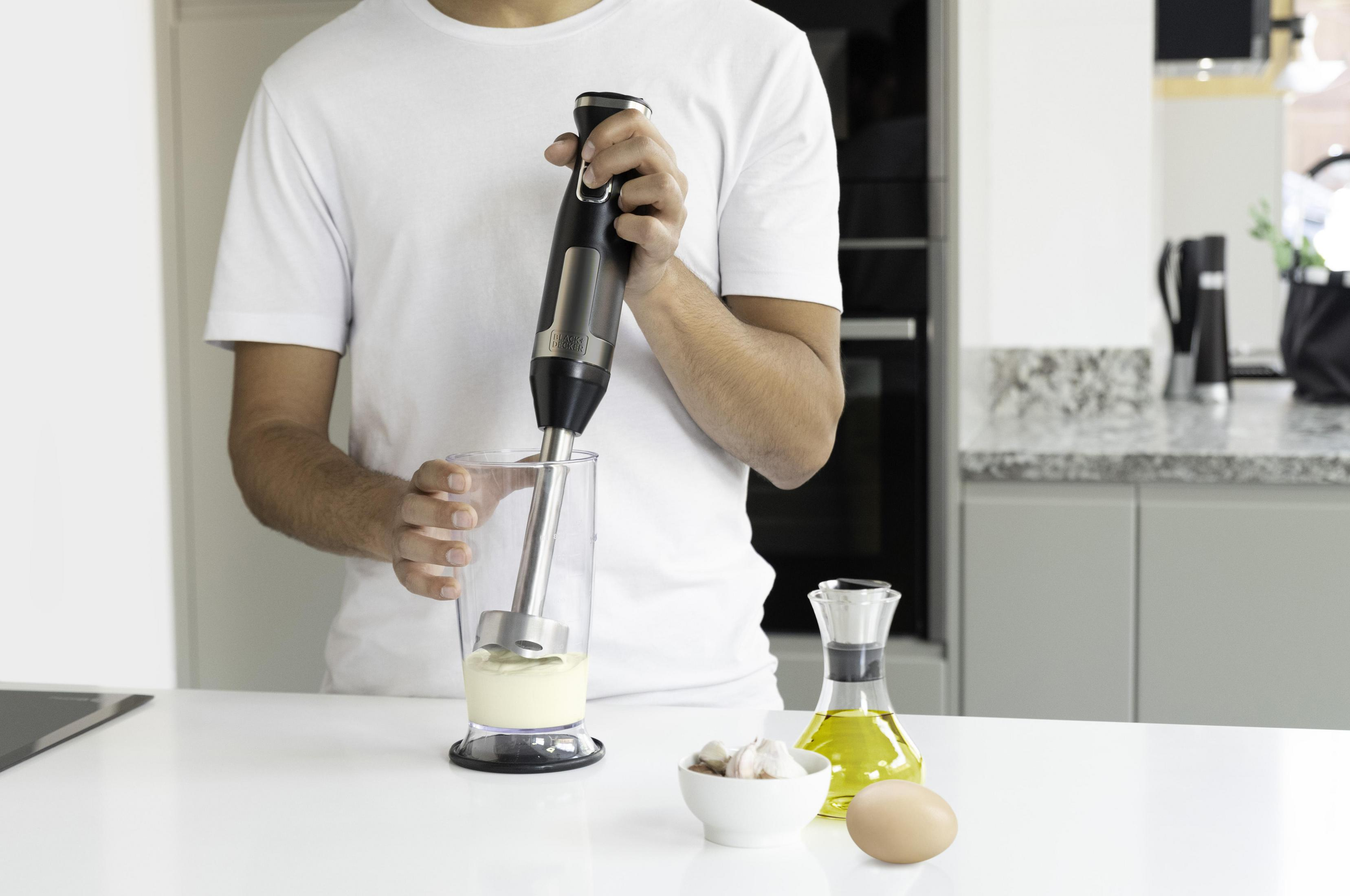 Osoba używająca blendera ręcznego w szklance. Składniki na blacie.