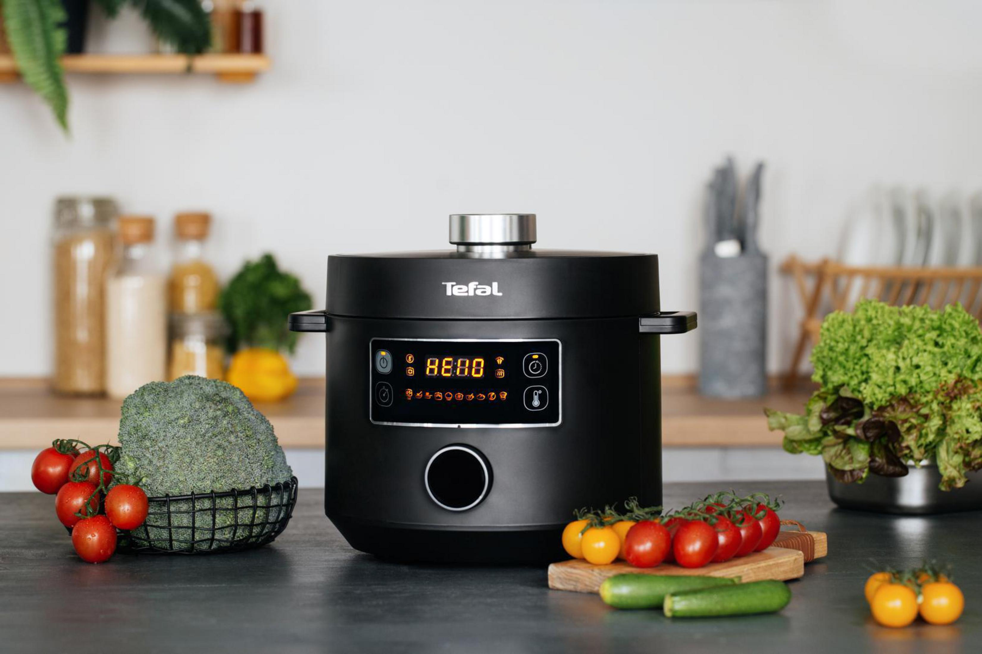 Ein schwarzer Tefal Multikocher auf einer Theke mit Gemüse, Tomaten und einem Küchenhintergrund.