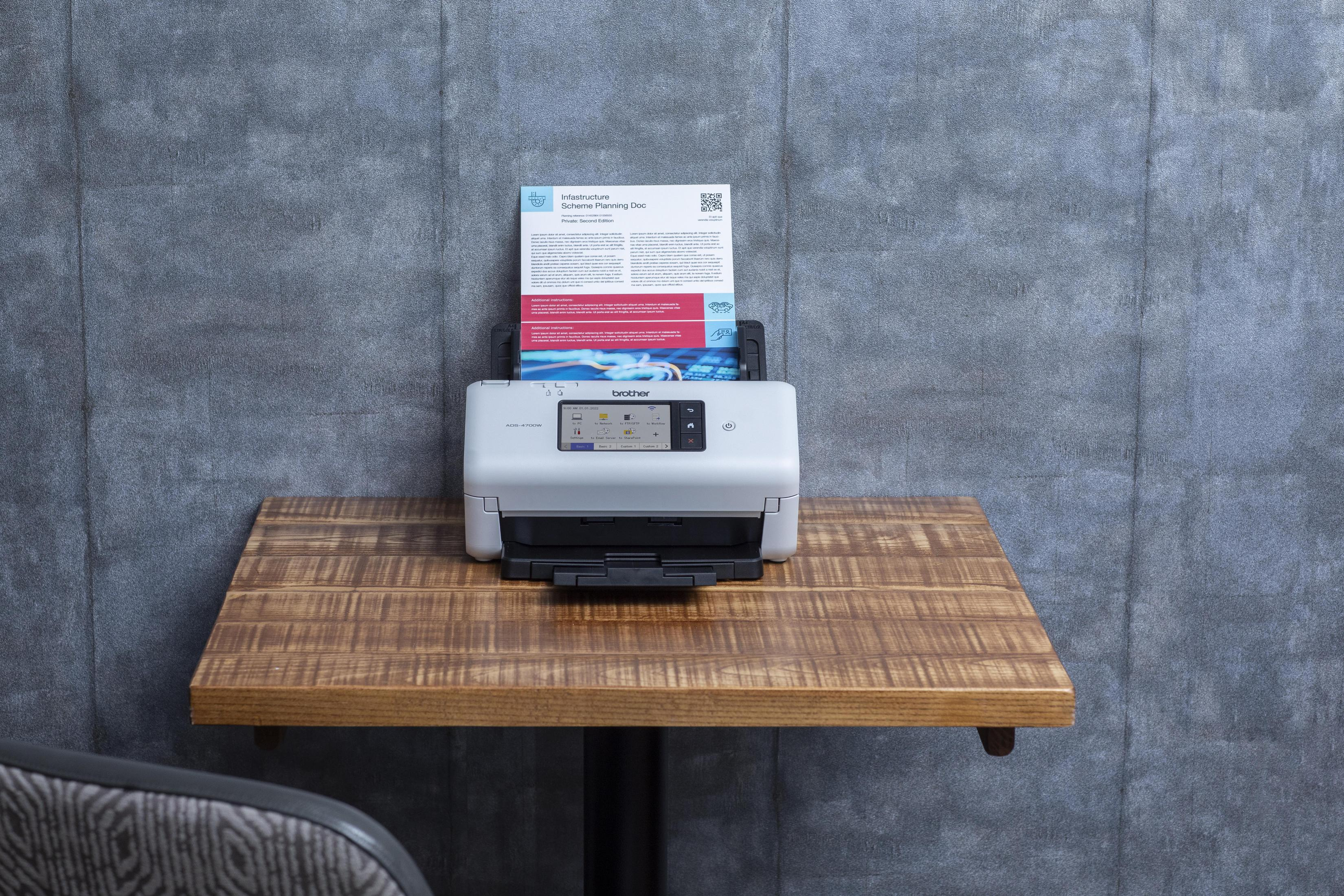 Biała drukarka z dokumentem w podajniku na drewnianej półce na szarej ścianie.