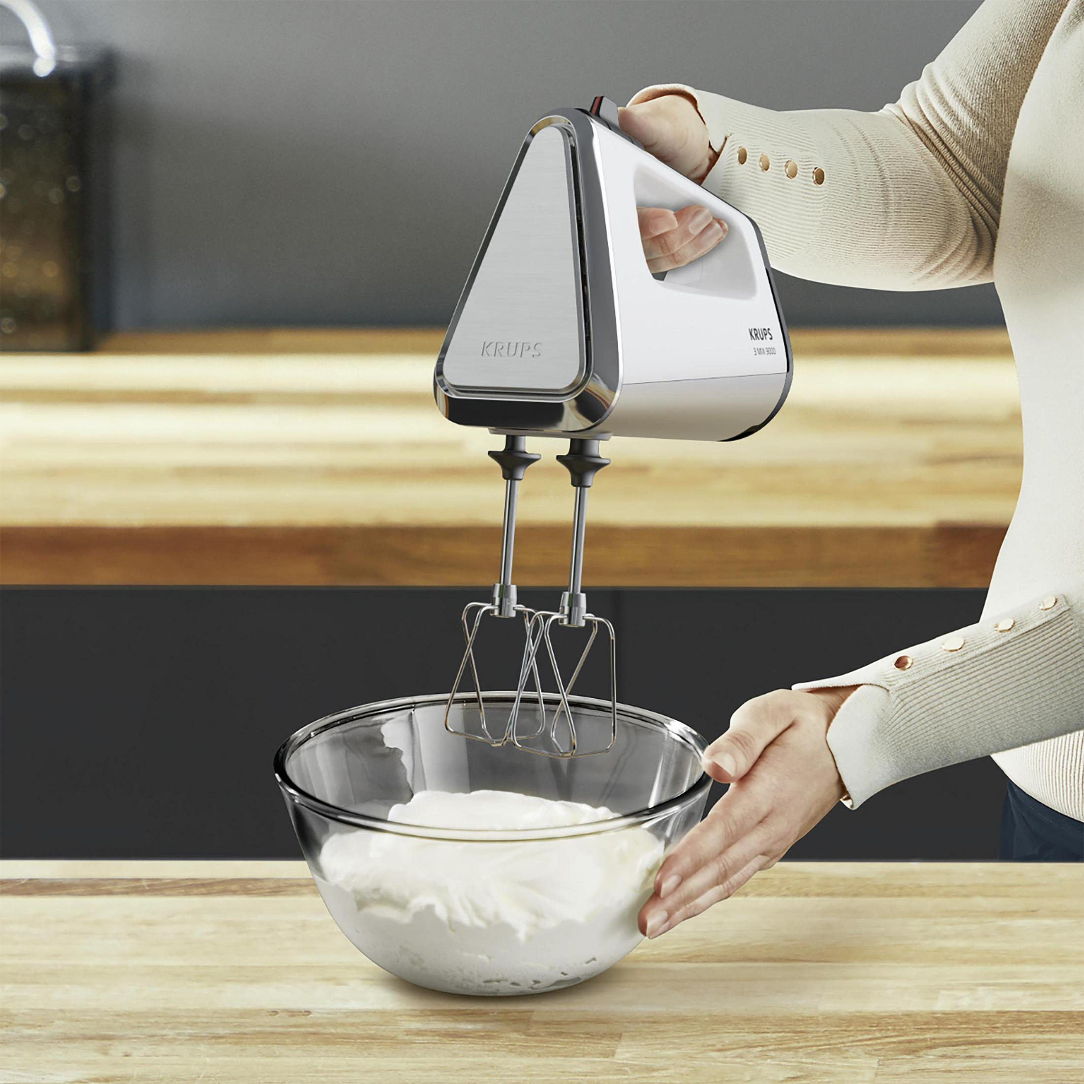 Frau benutzt weißen und silbernen Handmixer über einer Glasschüssel mit Sahne.
