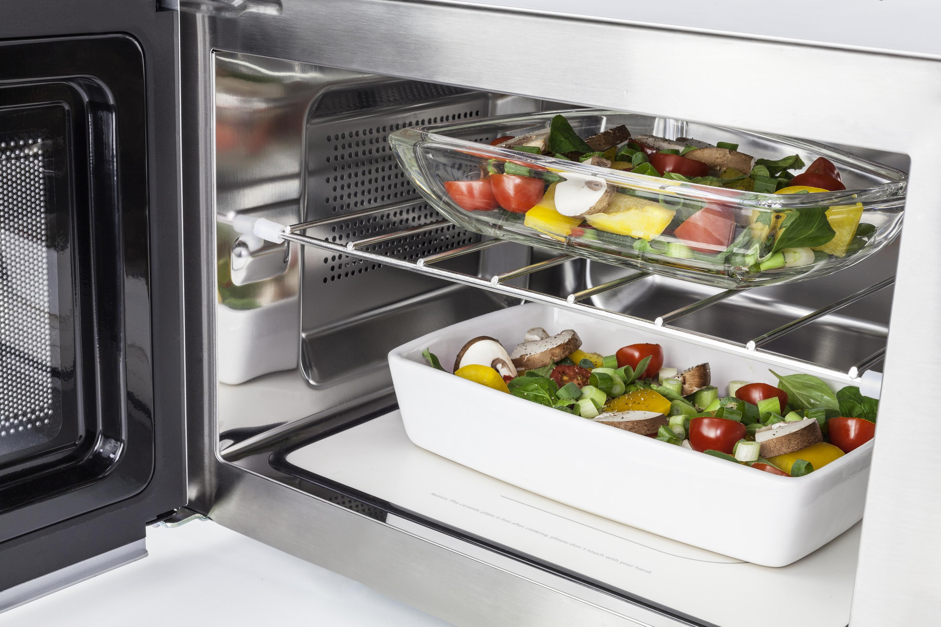 Un forno a microonde con la porta aperta che mostra due piatti di vetro con cibo. L'interno è in acciaio inossidabile.