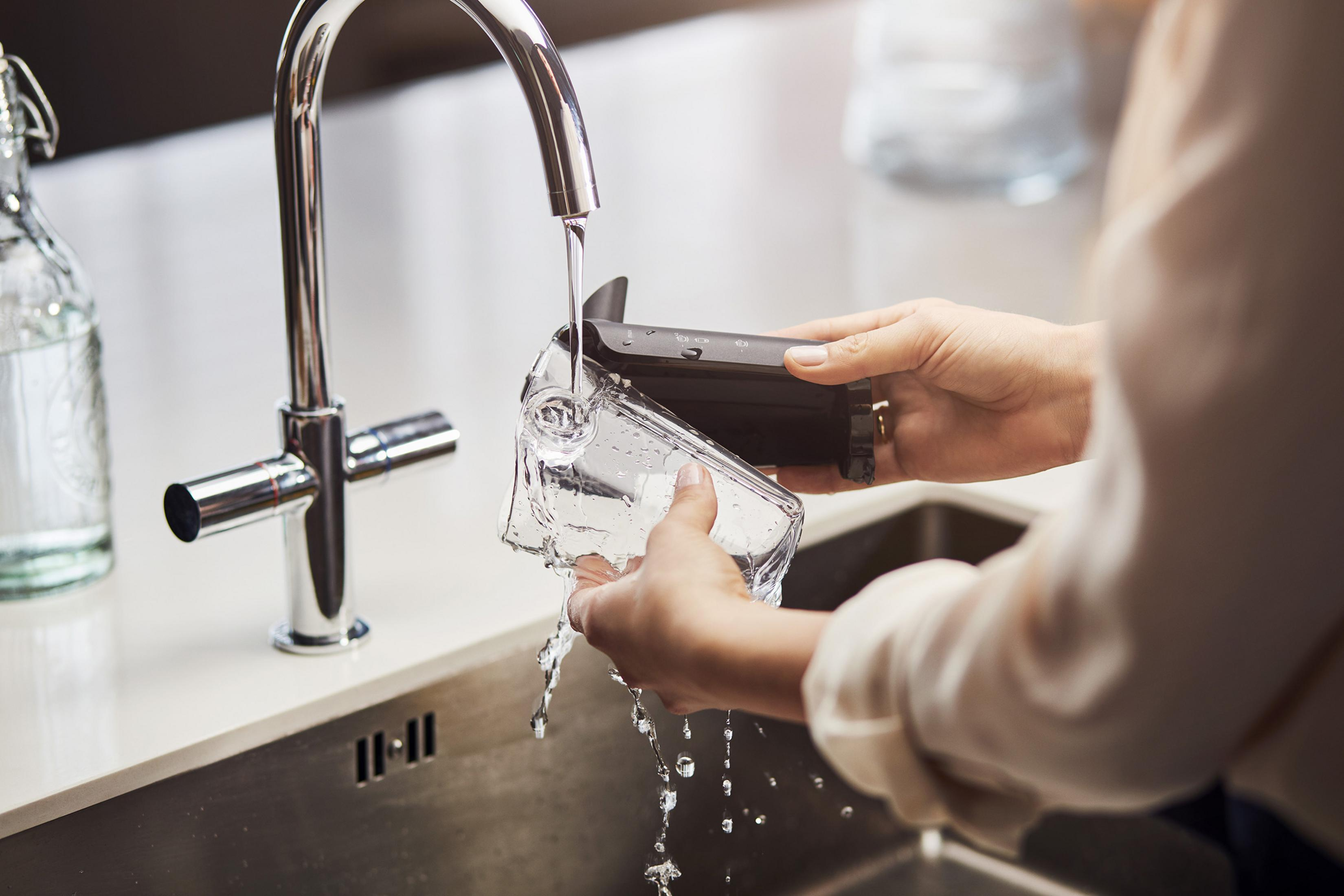 Mani che lavano un contenitore trasparente sotto l'acqua corrente.