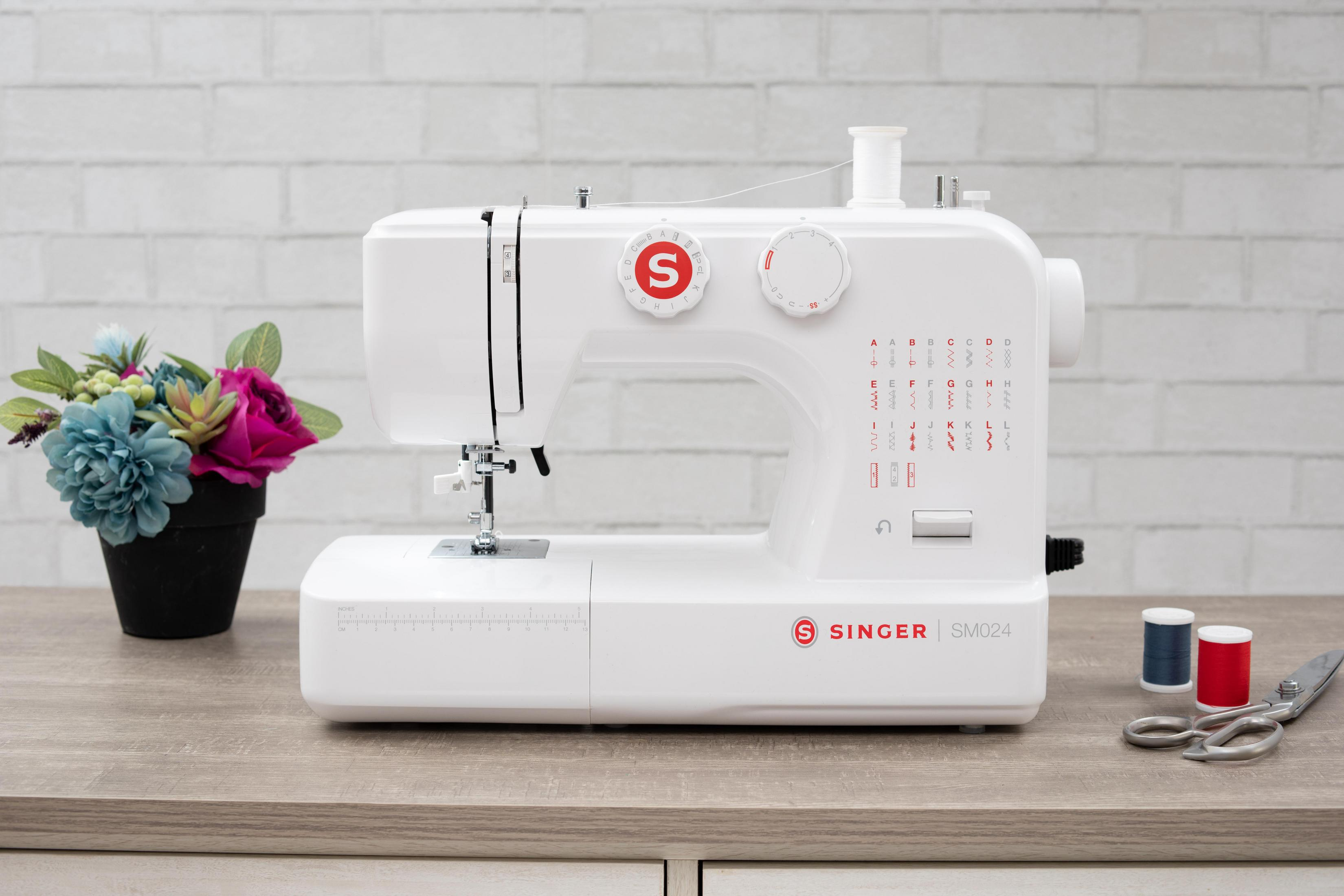 Biała maszyna do szycia Singer ze szpulkami nici i nożyczkami na drewnianym stole.