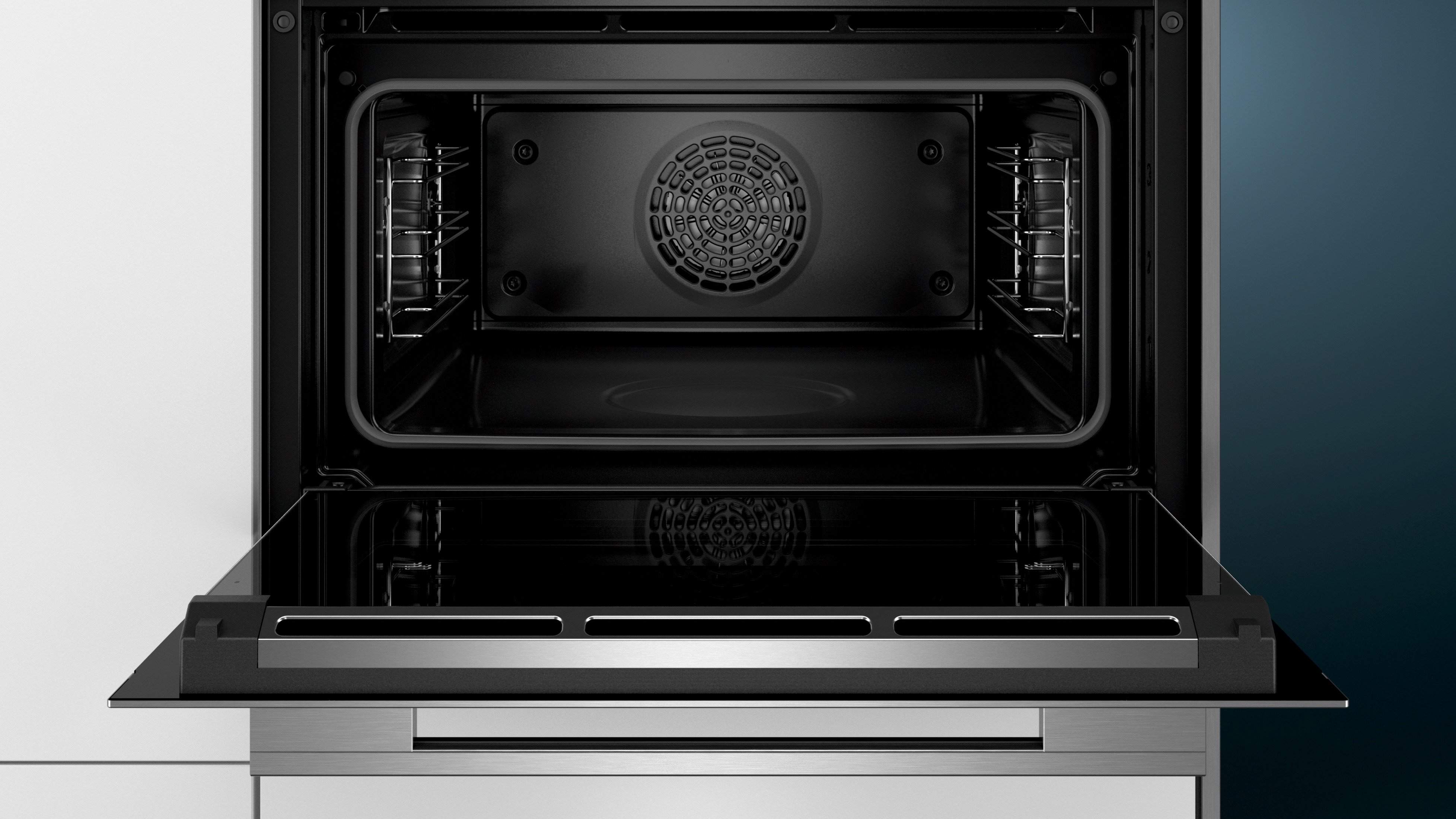Interior del horno abierto con el elemento calefactor y ventilador visibles, dentro de una cocina blanca.