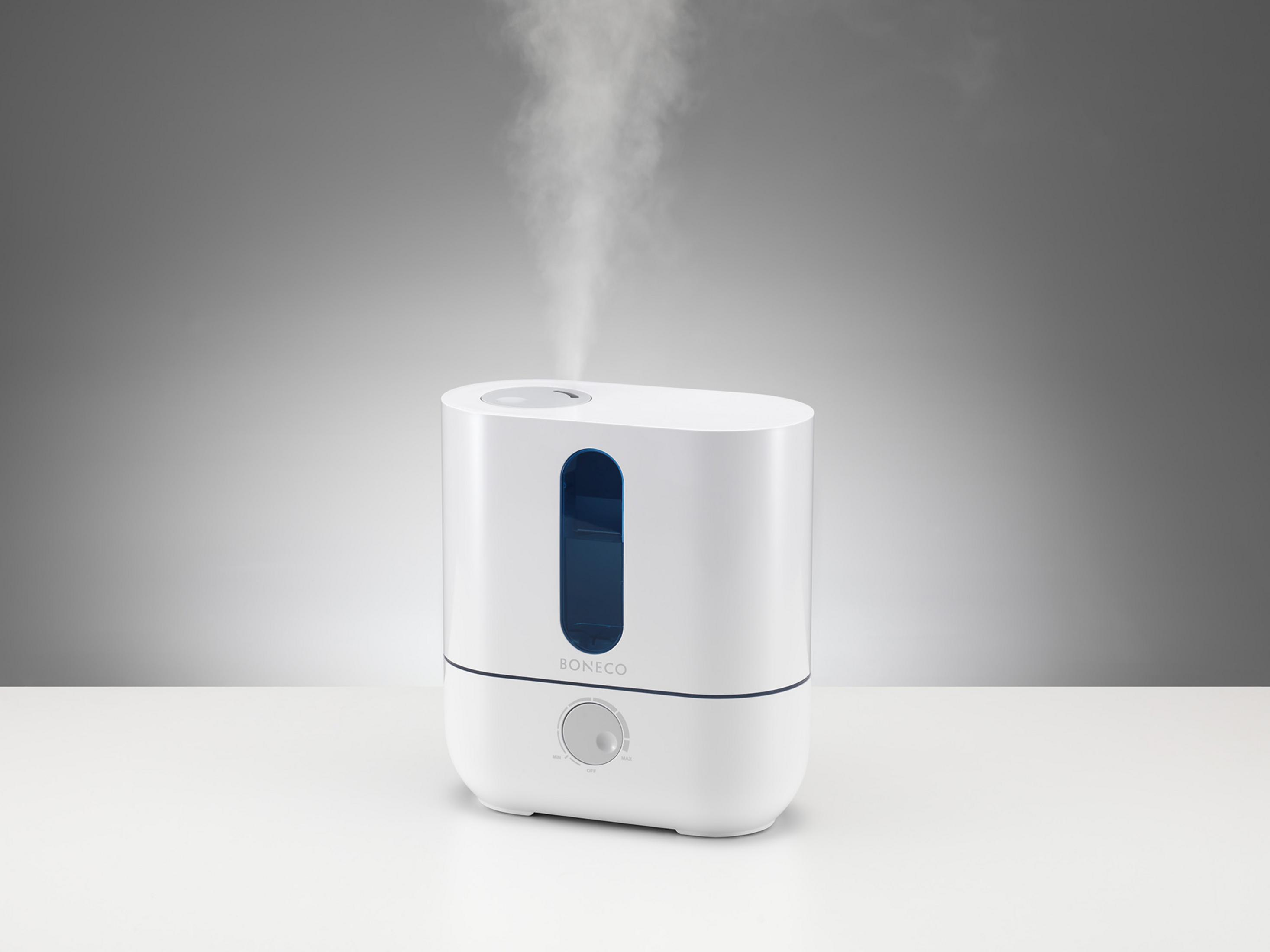 Un humidificador blanco emitiendo vapor. El fondo es un degradado de blanco y gris.
