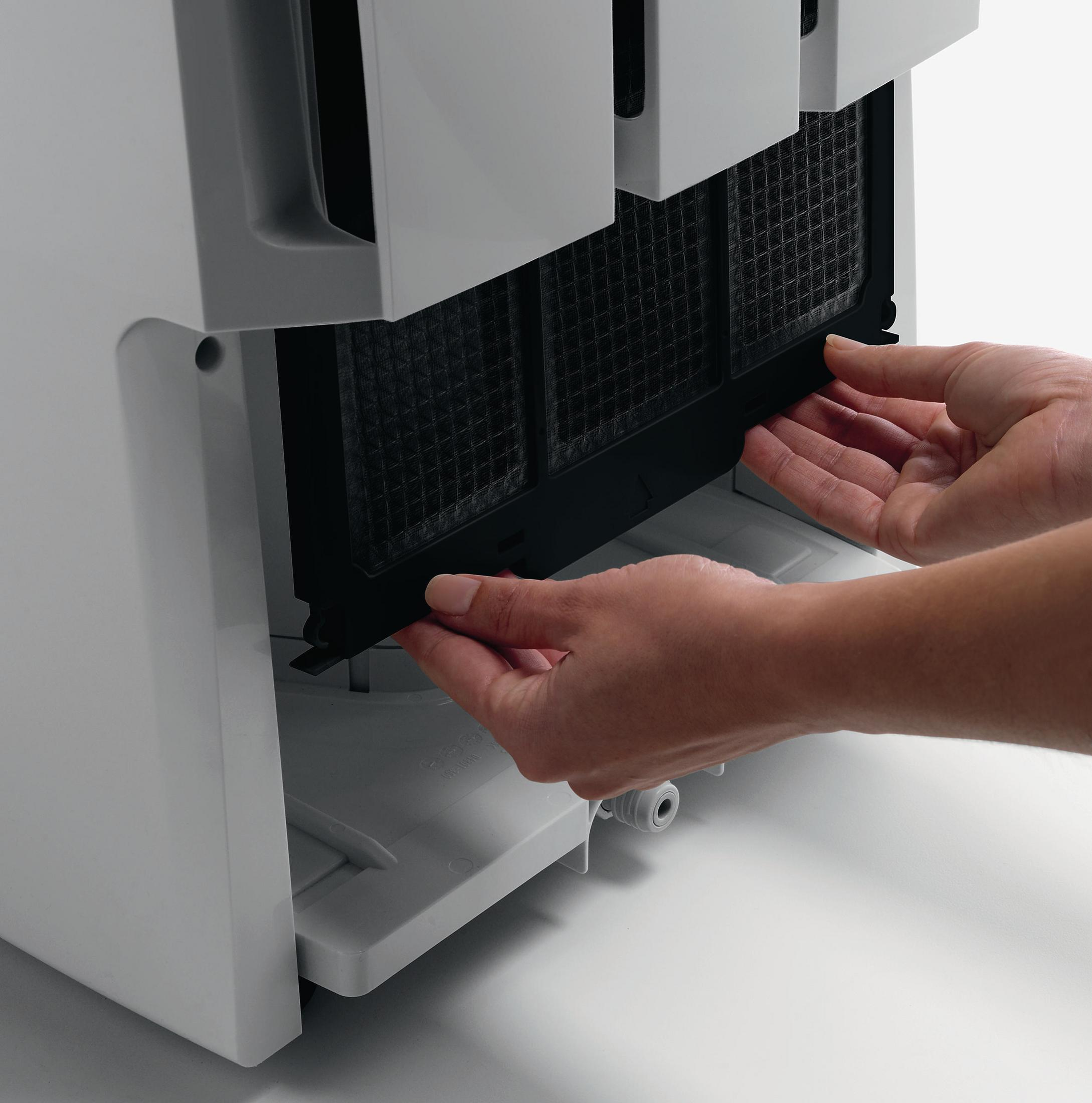 Ręce wyjmujące filtr z białego oczyszczacza powietrza. Filtr jest czarny.