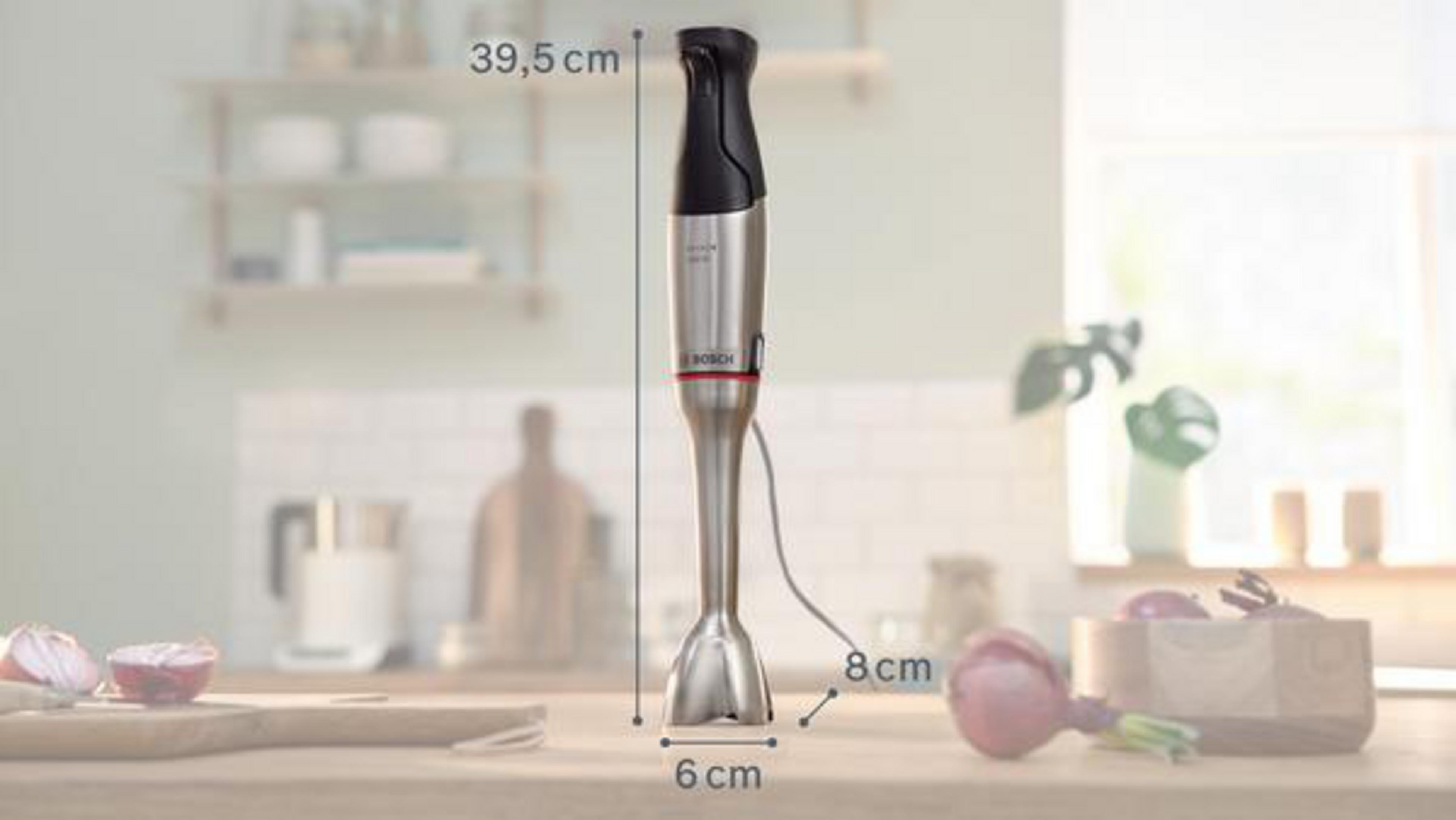 Stabmixer mit Maßen, auf einem Tisch in einer Küche, mit Gemüse im Hintergrund.