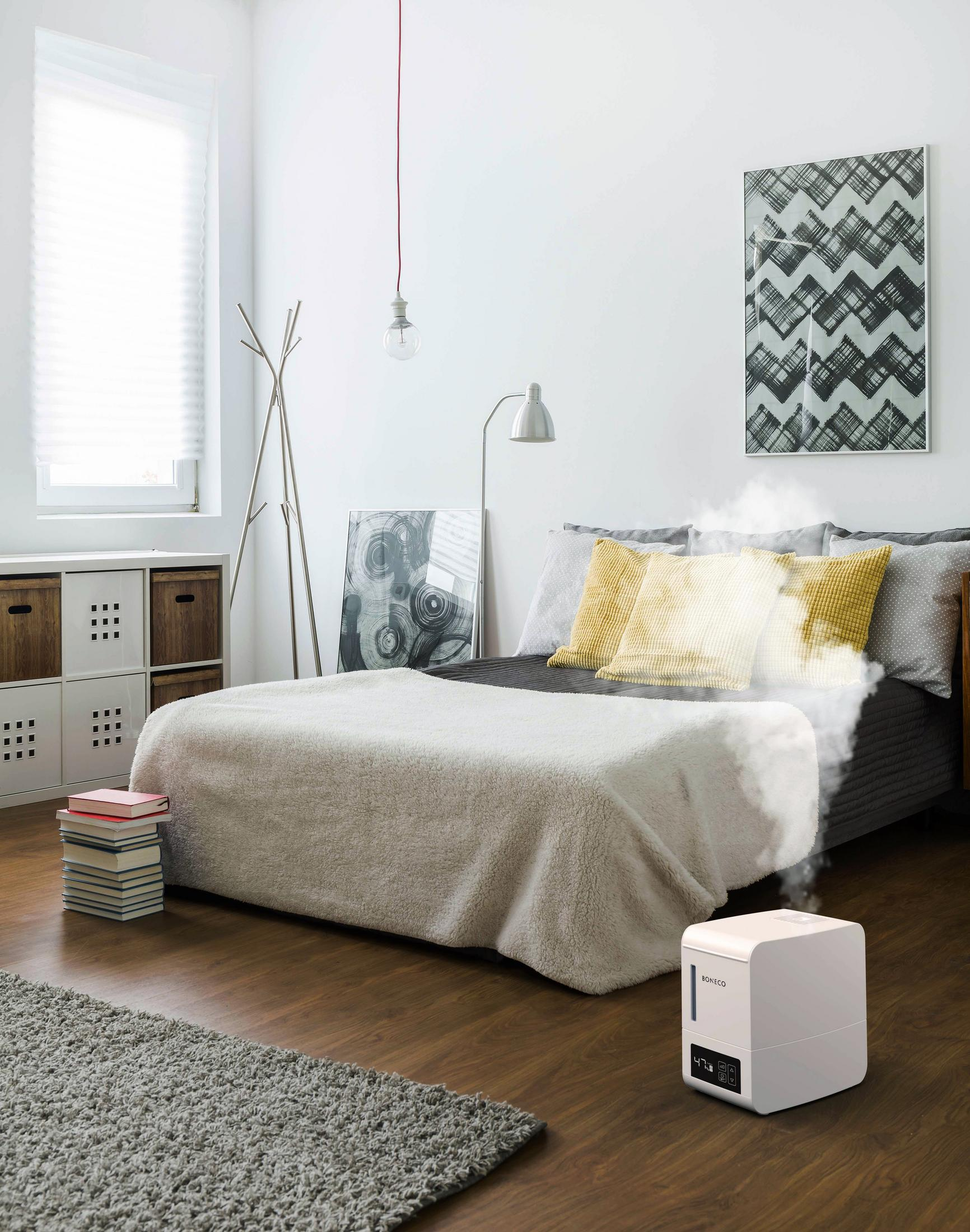 Camera da letto con umidificatore che emette vapore. Letto con cuscini, libri e tappeto.