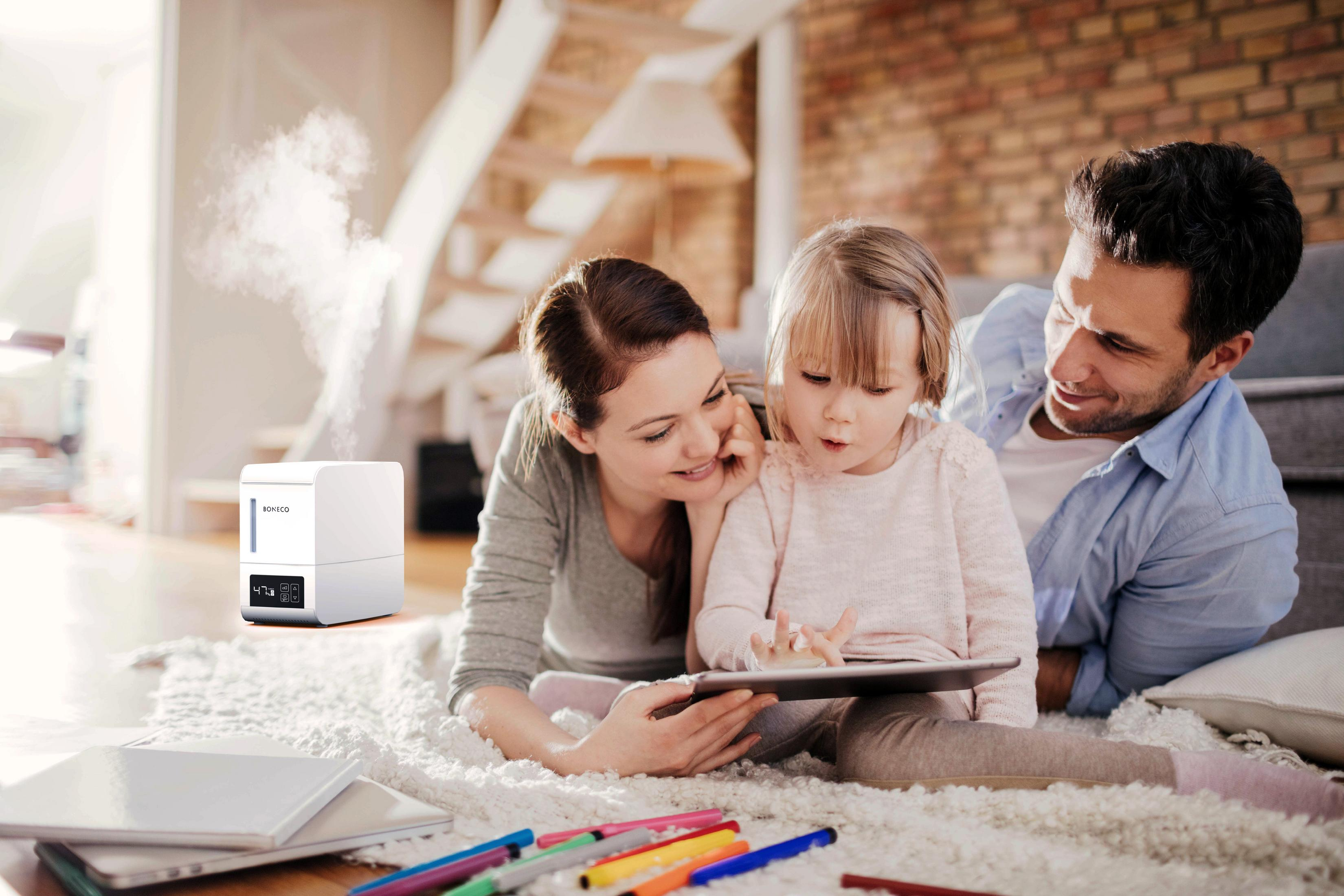 Famiglia con umidificatore, una bambina con un tablet e i genitori che la guardano.