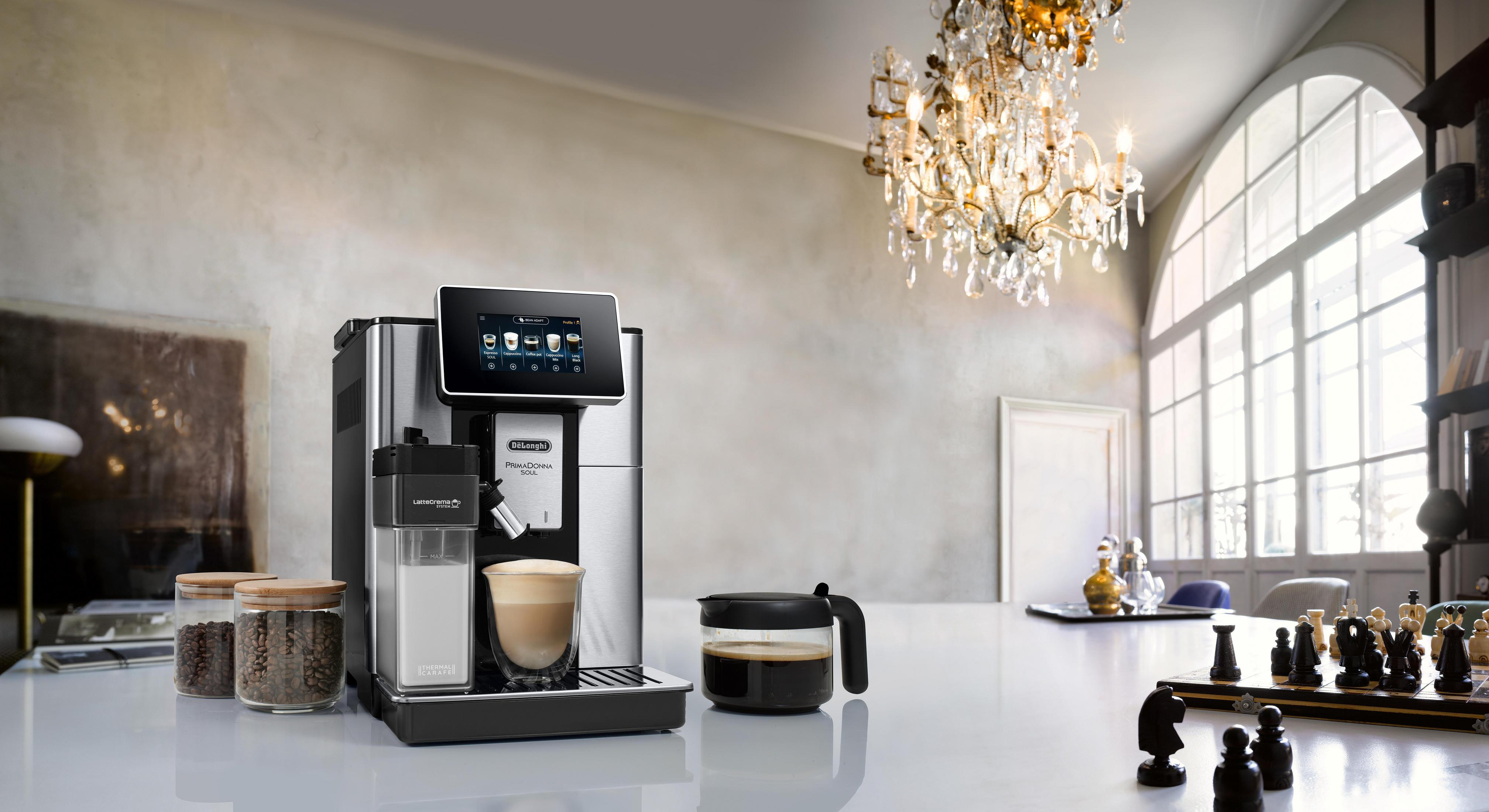 Eine DeLonghi Kaffeemaschine mit einem Glas Latte Macchiato, neben Kaffeebohnen.