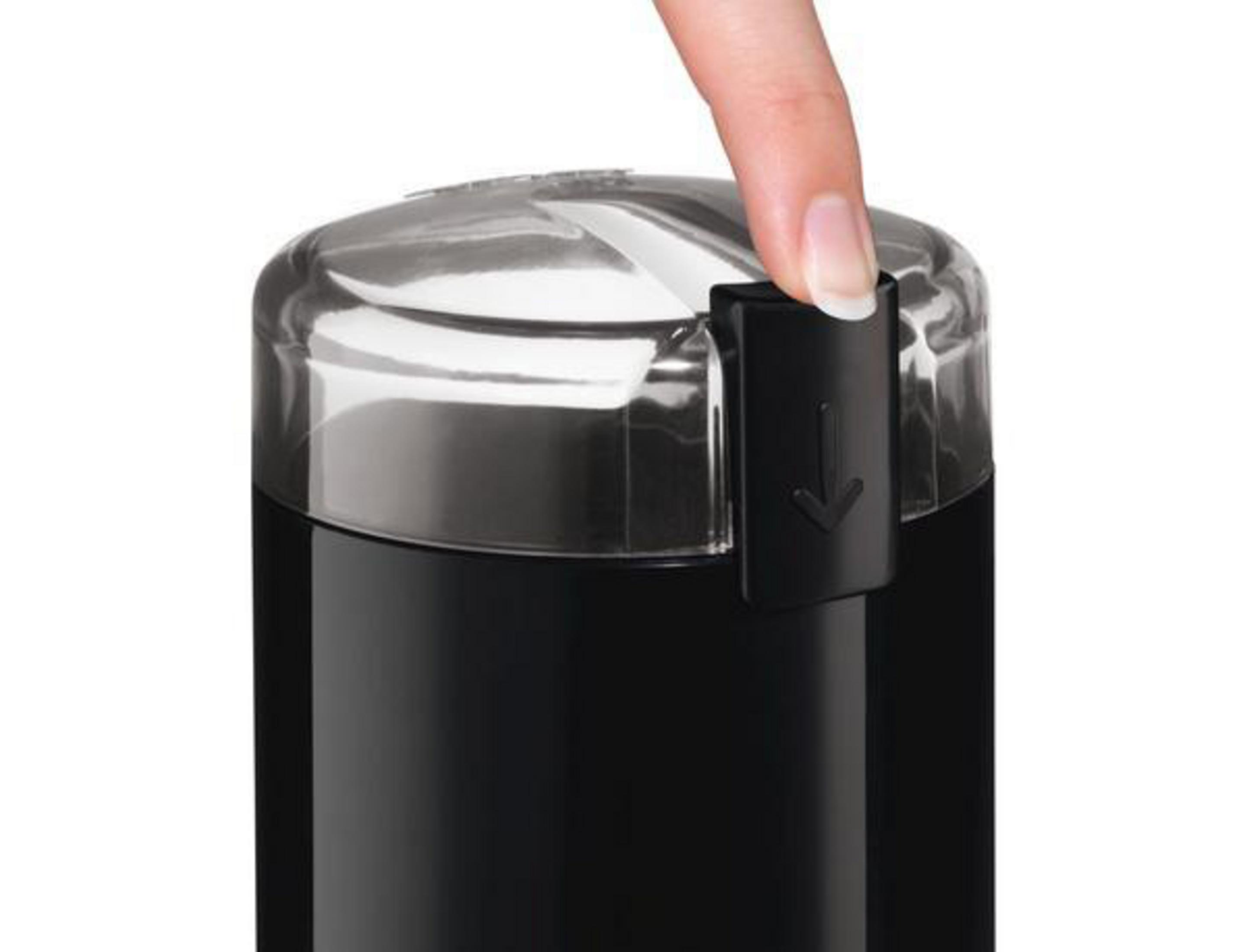 Close-up of a black coffee grinder with a button being pressed by a finger.
