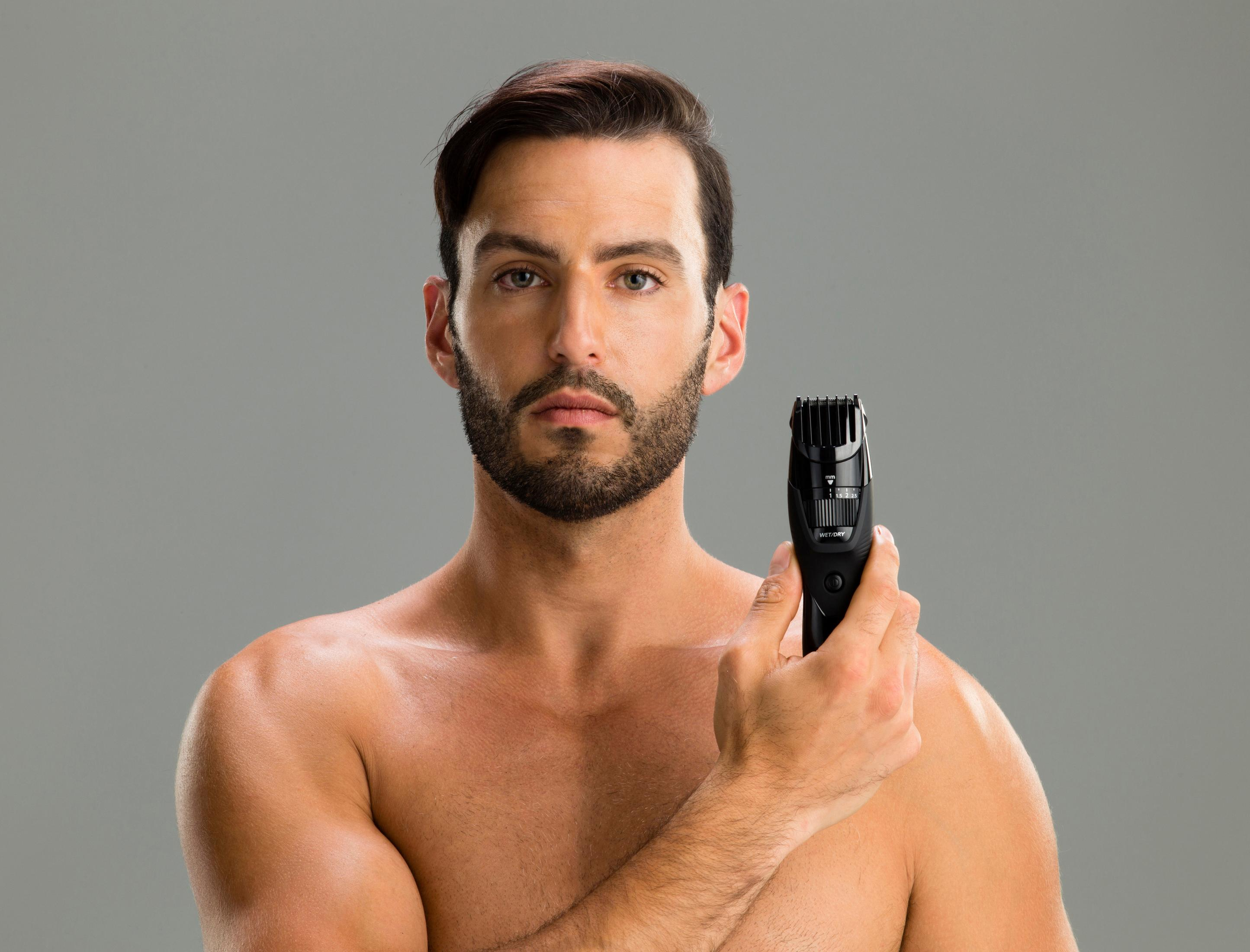 Homme tenant une tondeuse, torse nu, fond gris.